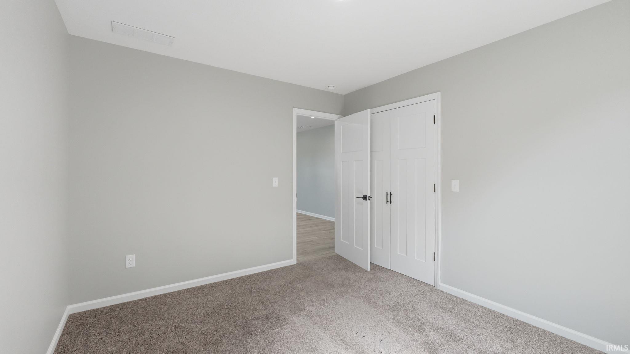 Neutral-toned room featuring light gray walls, plush carpeting, white baseboards, and a white interior door with black hardware