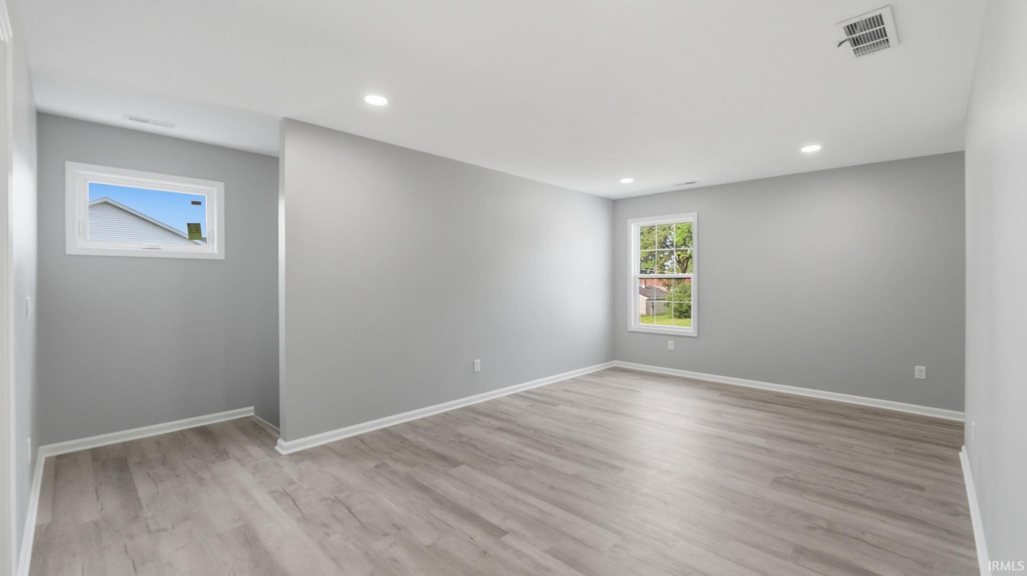 Spacious room featuring light gray walls, recessed lighting, and wood-finish flooring