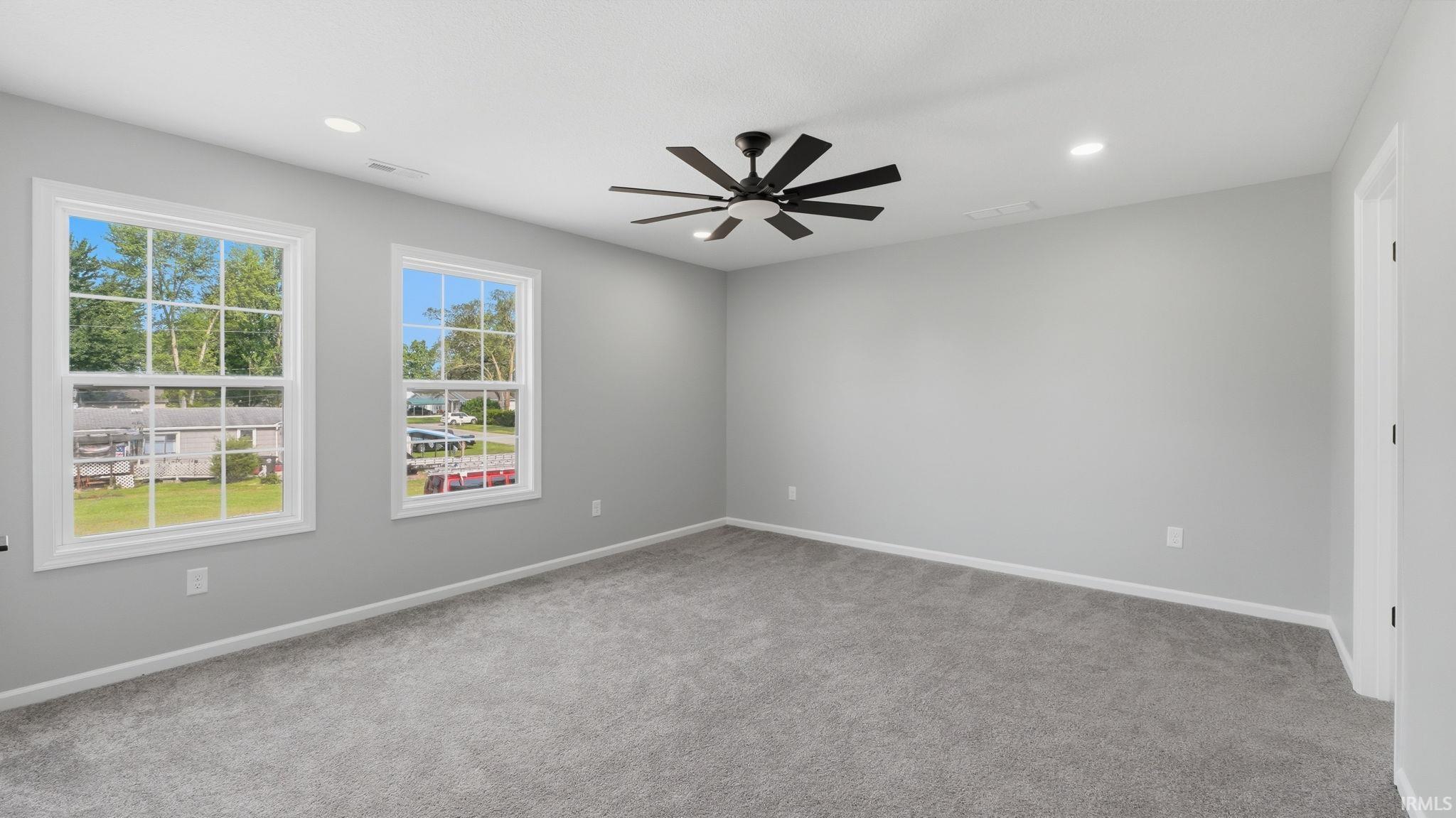 Spacious room featuring light gray walls, gray carpeting, a contemporary black ceiling fan, recessed lighting, and two large windows with white frames