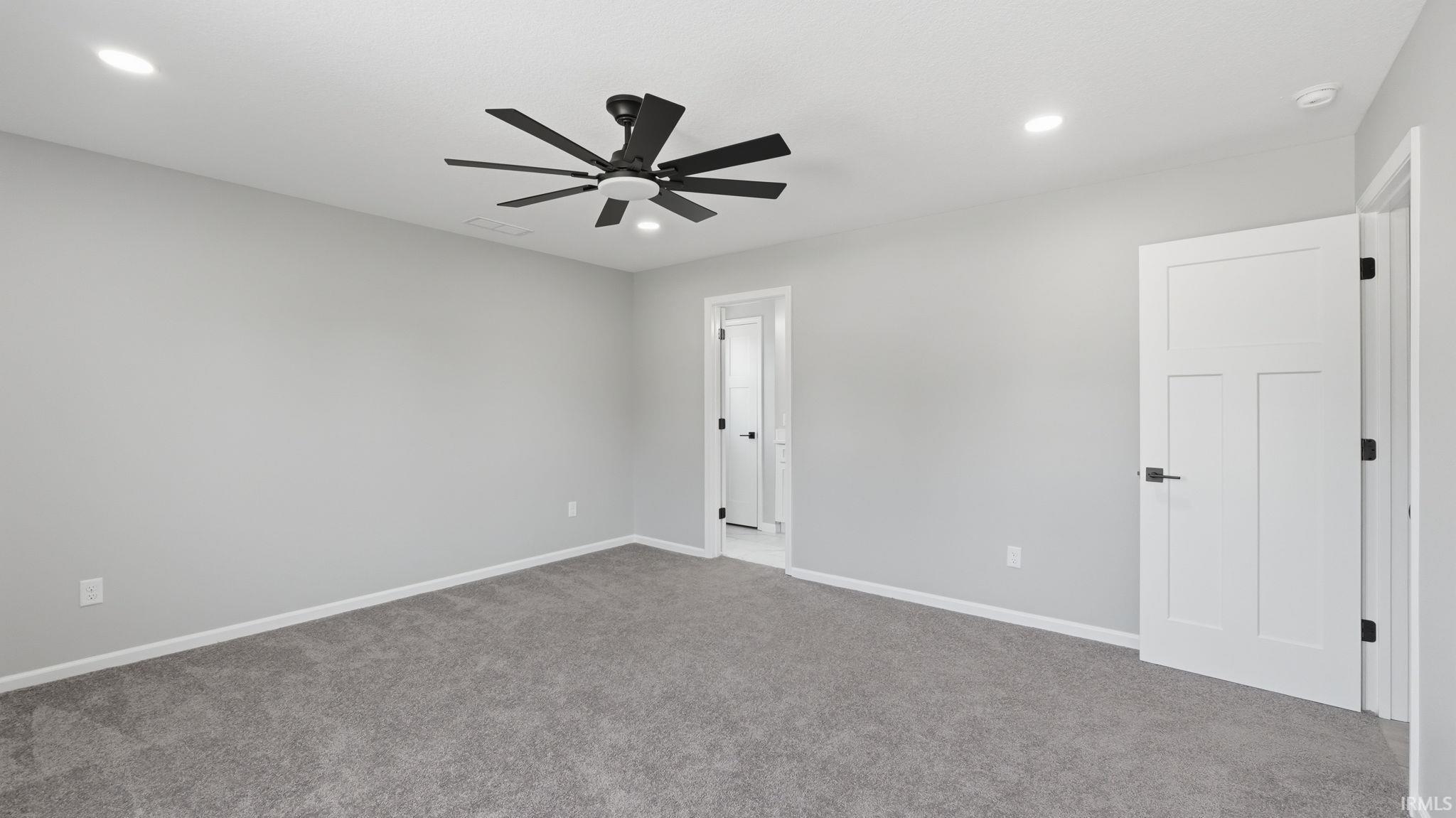 Spacious room featuring gray carpeting, light gray walls, a modern black ceiling fan, recessed lighting, and a white interior door with black hardware
