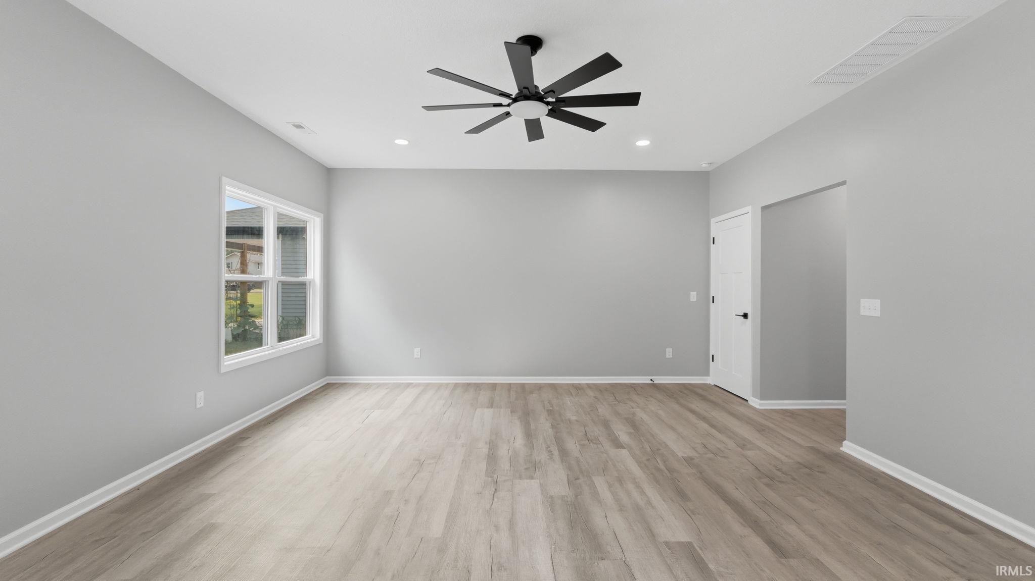 Spacious room featuring light wood-finish flooring, a contemporary black ceiling fan with multiple blades, recessed lighting, and a double-pane window providing natural light