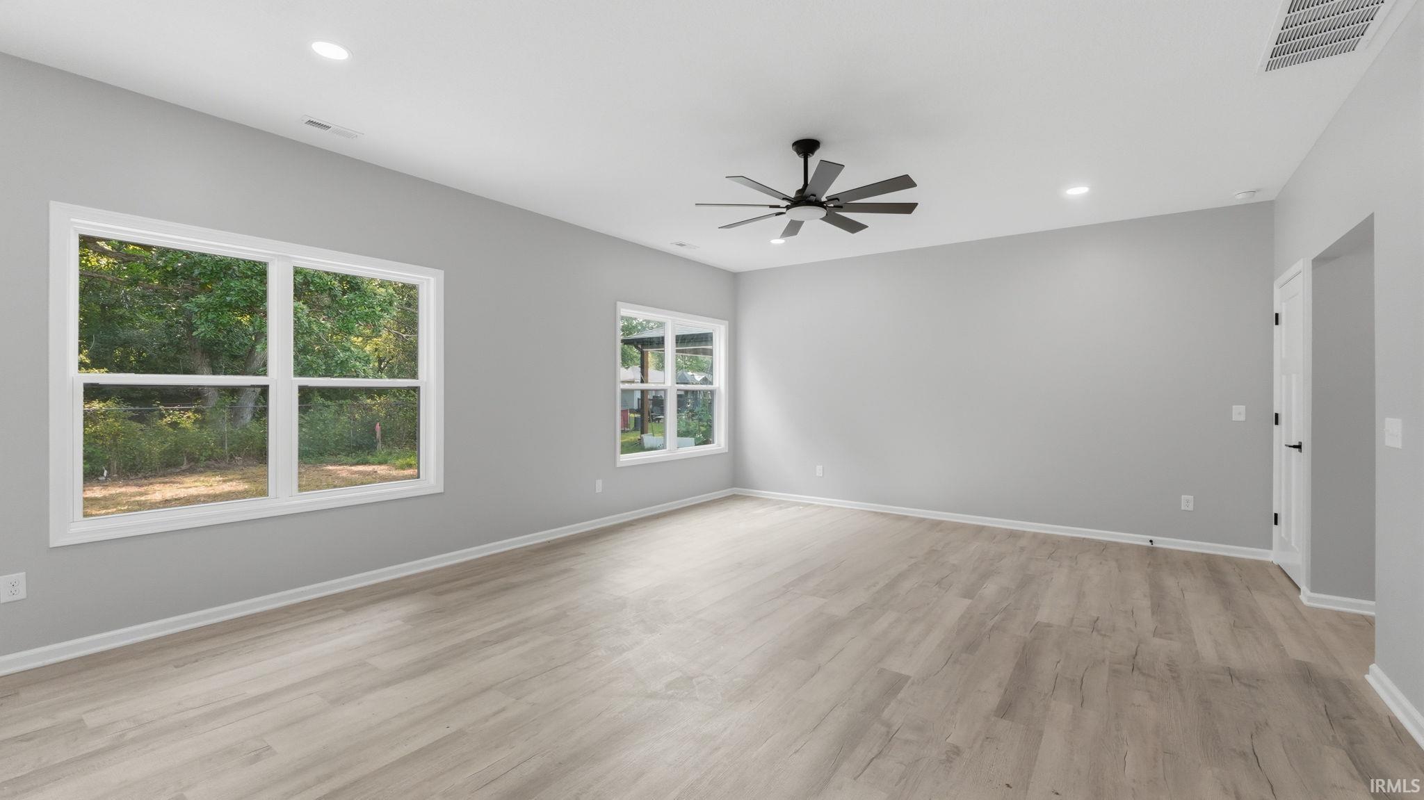 Spacious interior room featuring light wood-finish flooring, neutral gray wall paint, and white trim