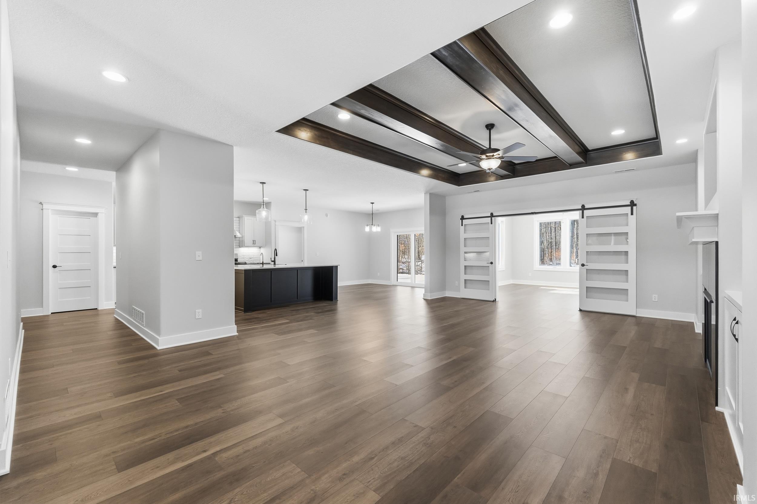 Unfurnished living room featuring a barn door, beamed ceiling, ceiling fan, a chandelier, and recessed lighting