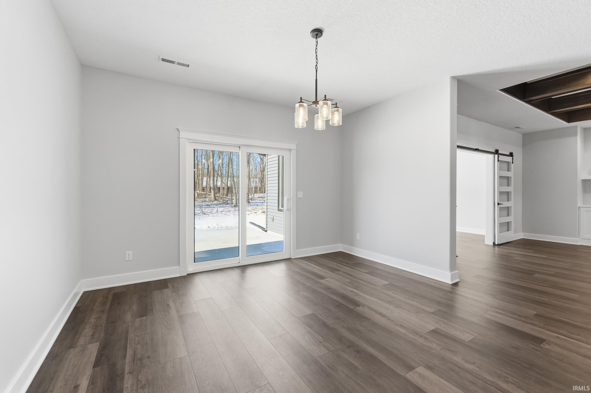 Unfurnished dining area featuring a barn door, a chandelier, and dark wood-style floors