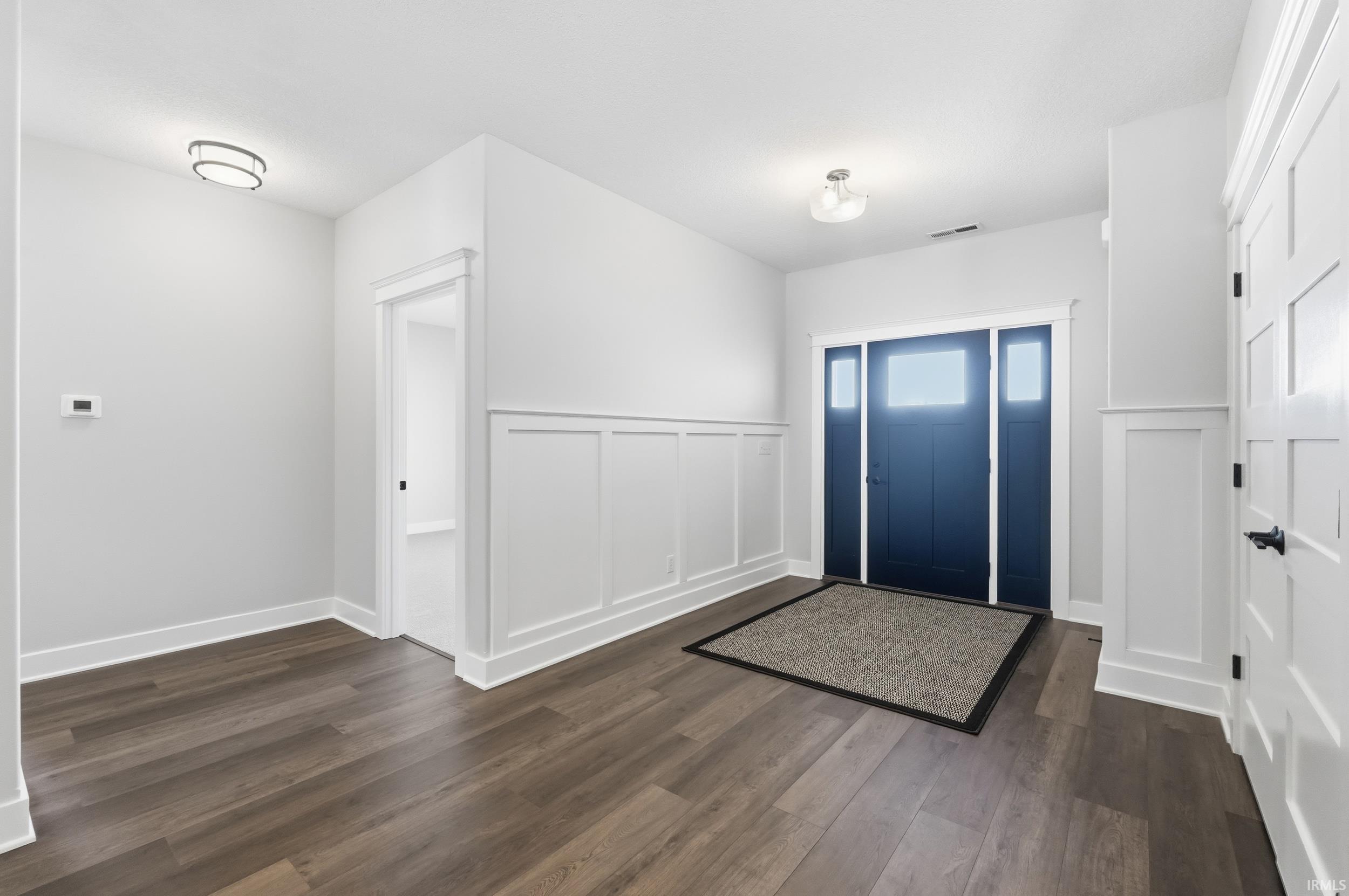 Foyer with dark wood finished floors, a decorative wall, and wainscoting