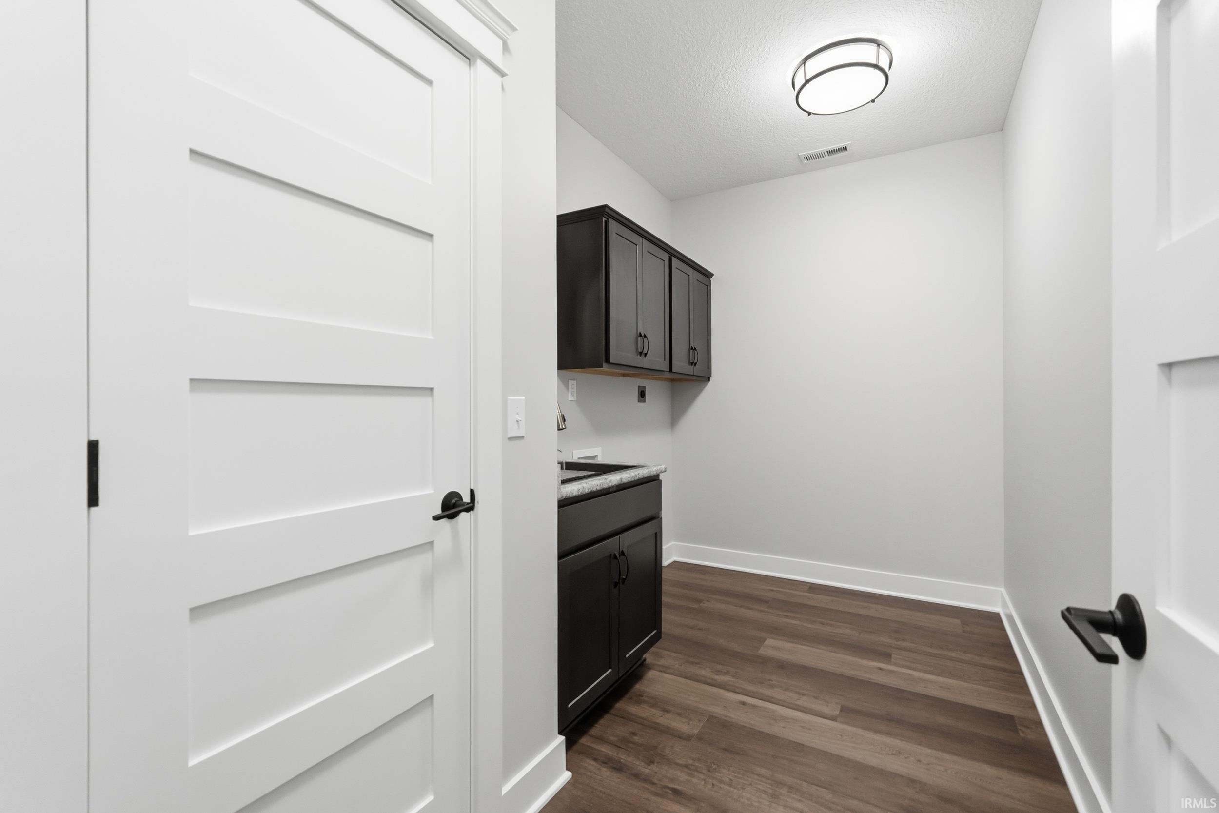 Washroom featuring dark wood-type flooring, a textured ceiling, washer hookup, and cabinet space
