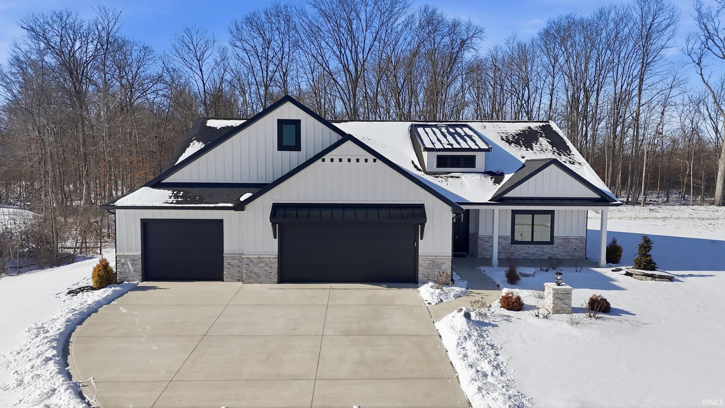 Modern inspired farmhouse with stone siding, concrete driveway, board and batten siding, and a garage