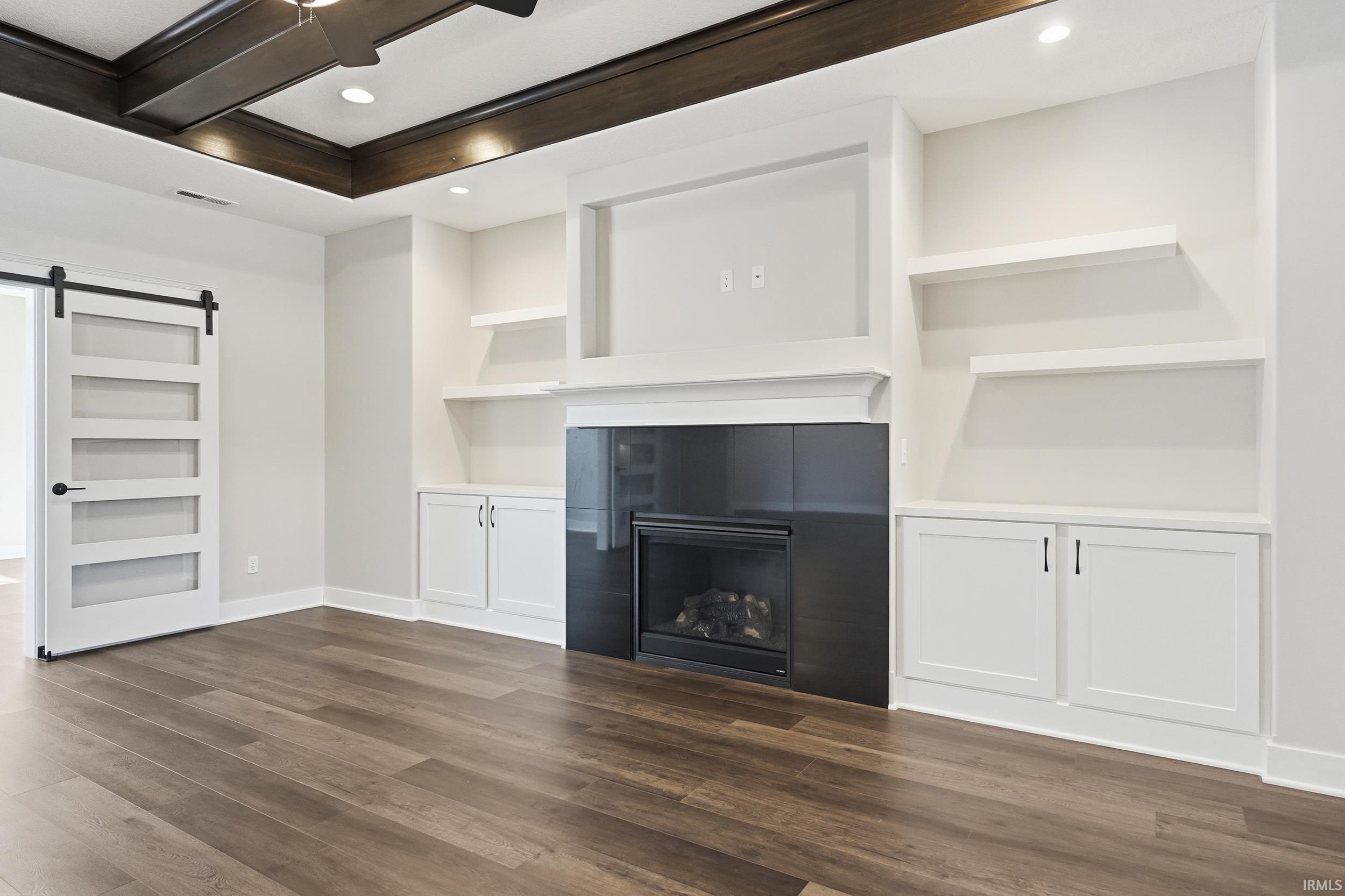Unfurnished living room featuring a barn door, built in shelves, a fireplace, dark wood-type flooring, and recessed lighting