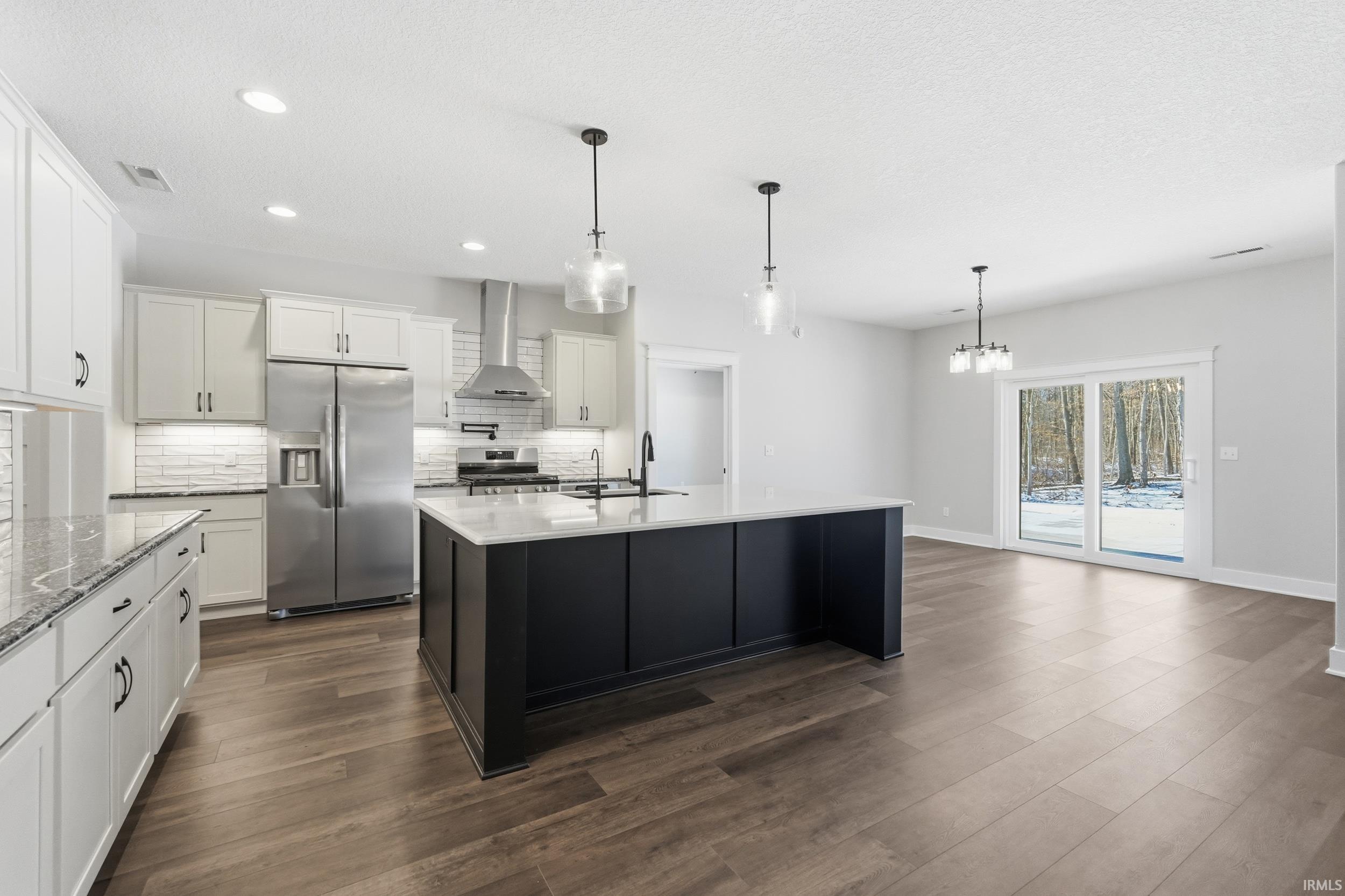 Kitchen with white cabinetry, appliances with stainless steel finishes, a kitchen island with sink, pendant lighting, and a textured ceiling
