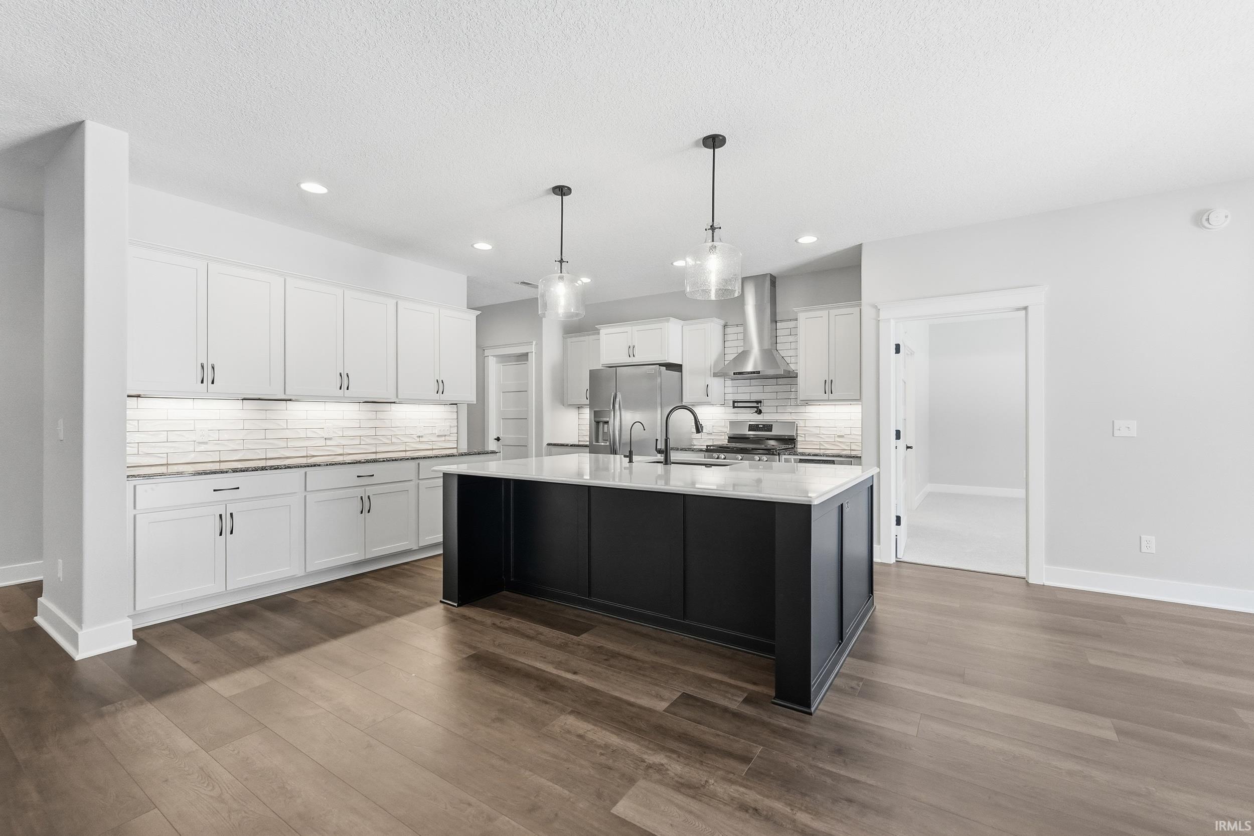 Kitchen featuring white cabinetry, pendant lighting, a center island with sink, dark cabinets, and stainless steel appliances