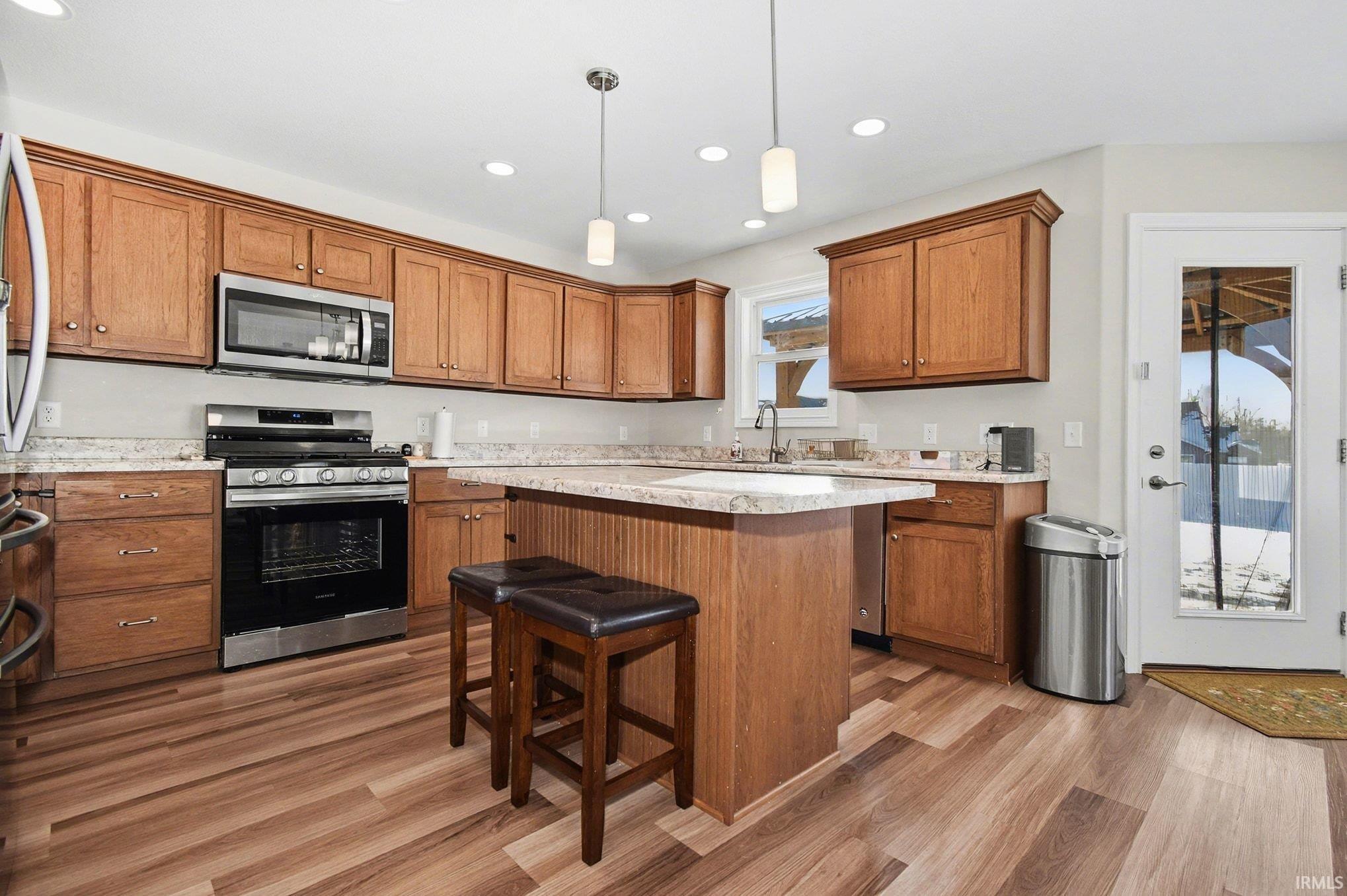 Kitchen with stainless steel appliances, a breakfast bar, recessed lighting, brown cabinets, and decorative light fixtures