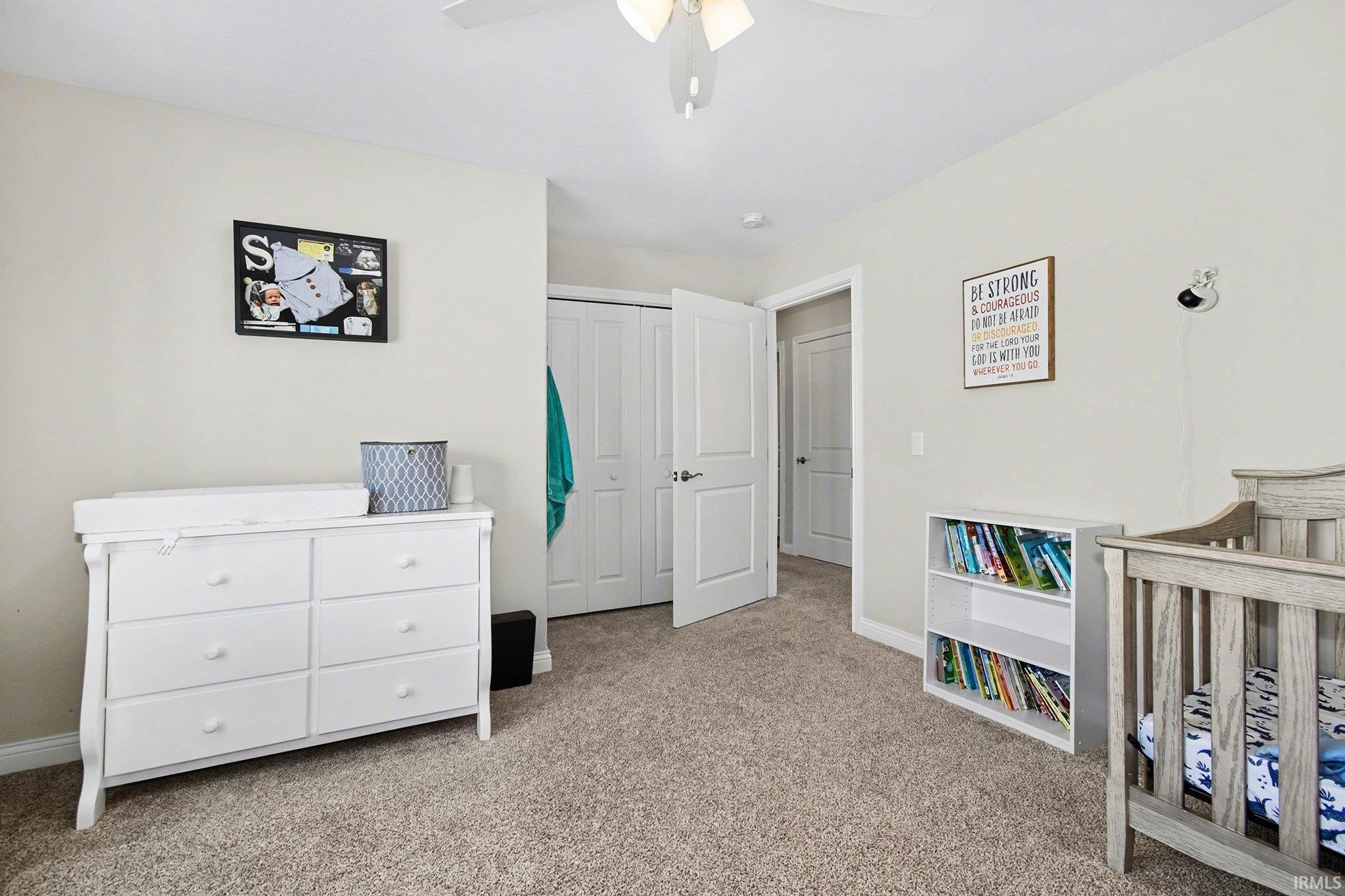 Bedroom featuring a crib, light carpet, a closet, and a ceiling fan