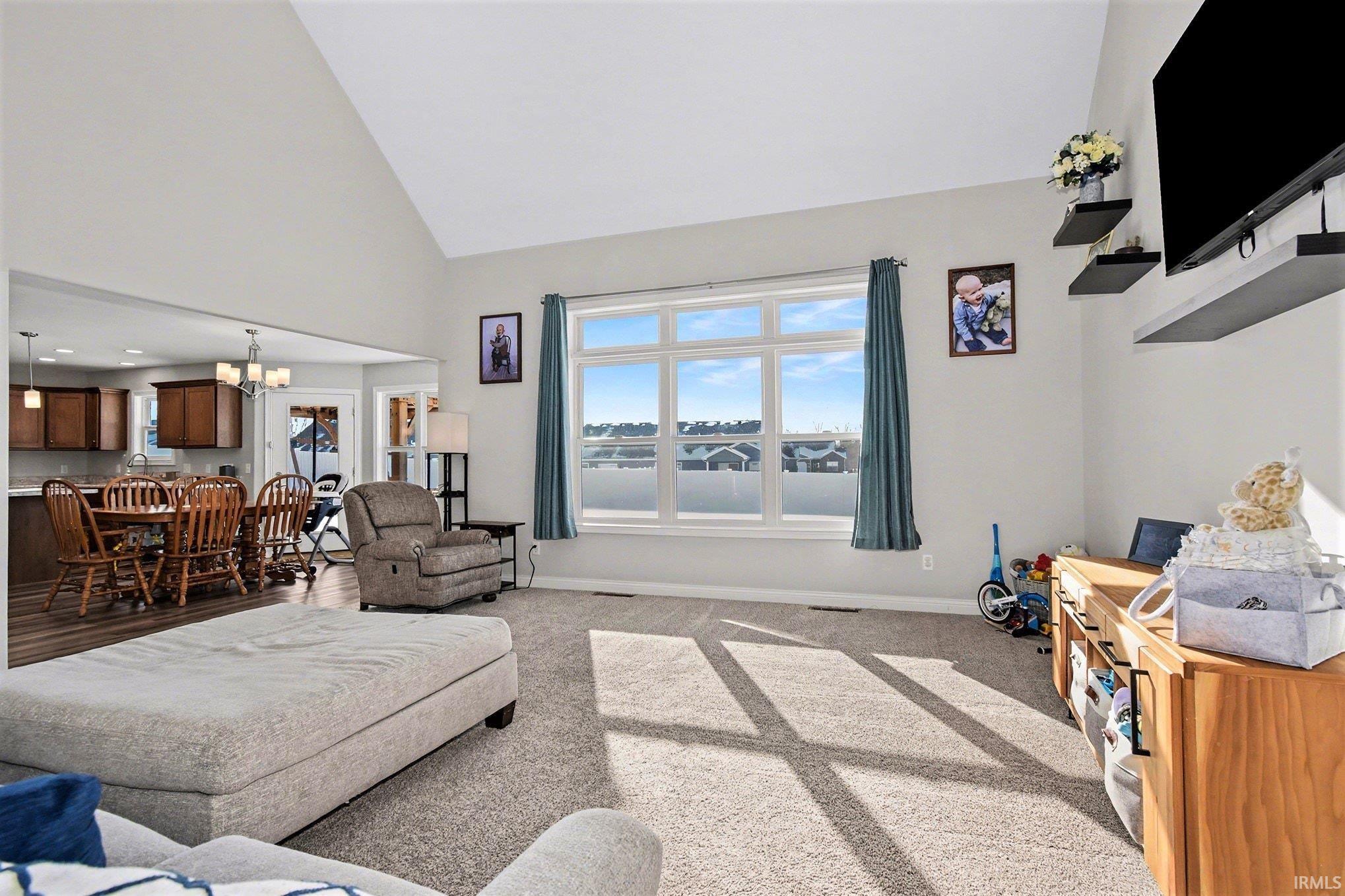 Carpeted living area with high vaulted ceiling and a chandelier