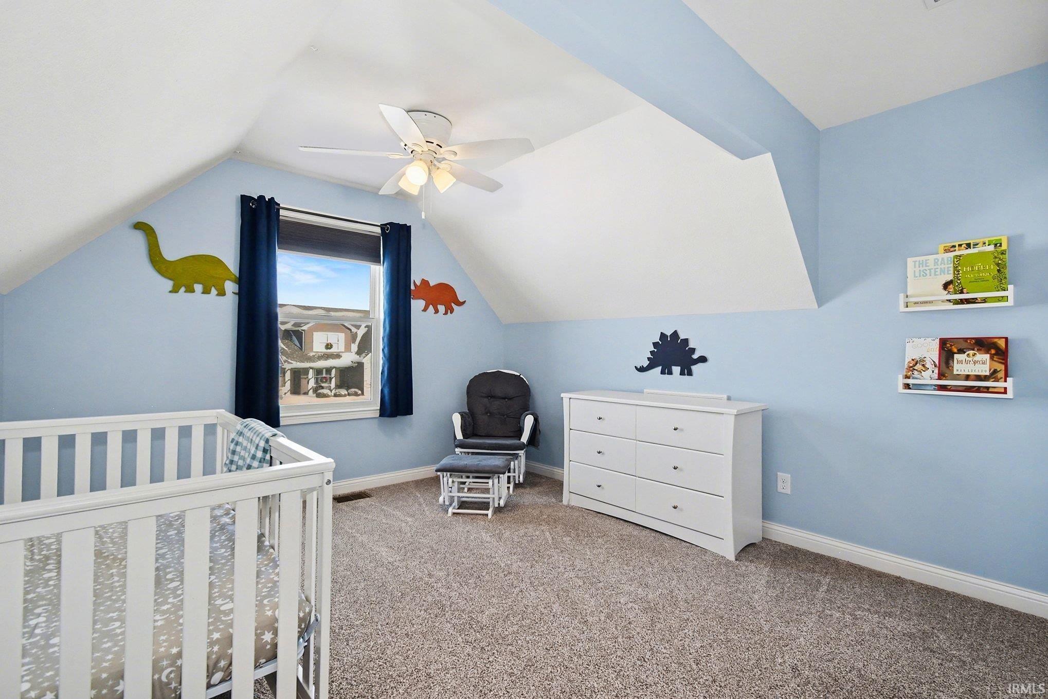 Bedroom featuring a crib, carpet floors, vaulted ceiling, and ceiling fan