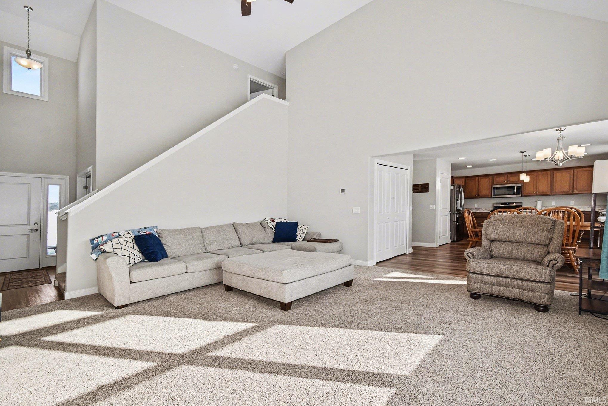 Living room featuring high vaulted ceiling, light carpet, a chandelier, and stairs