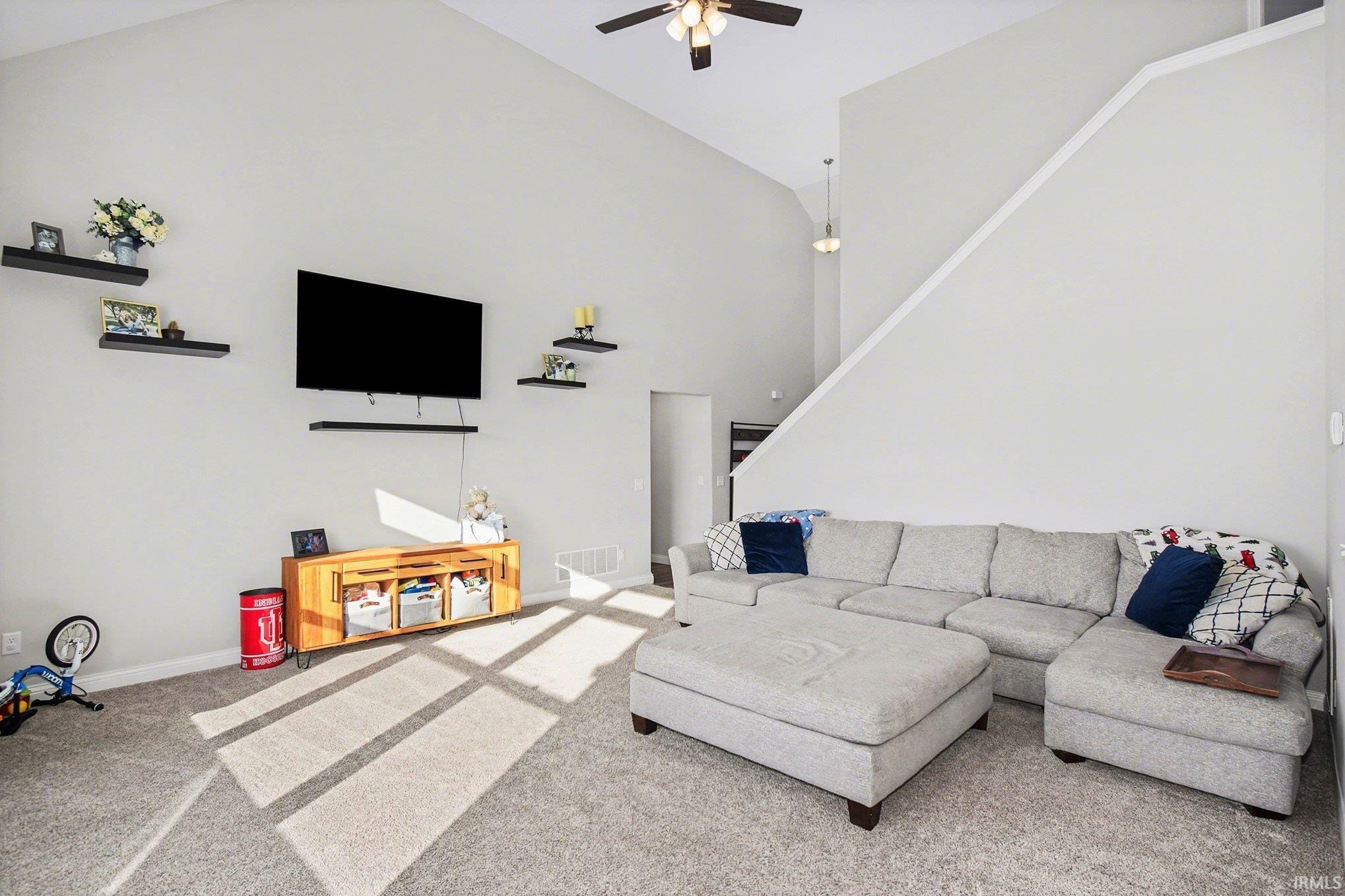 Carpeted living room with high vaulted ceiling and ceiling fan