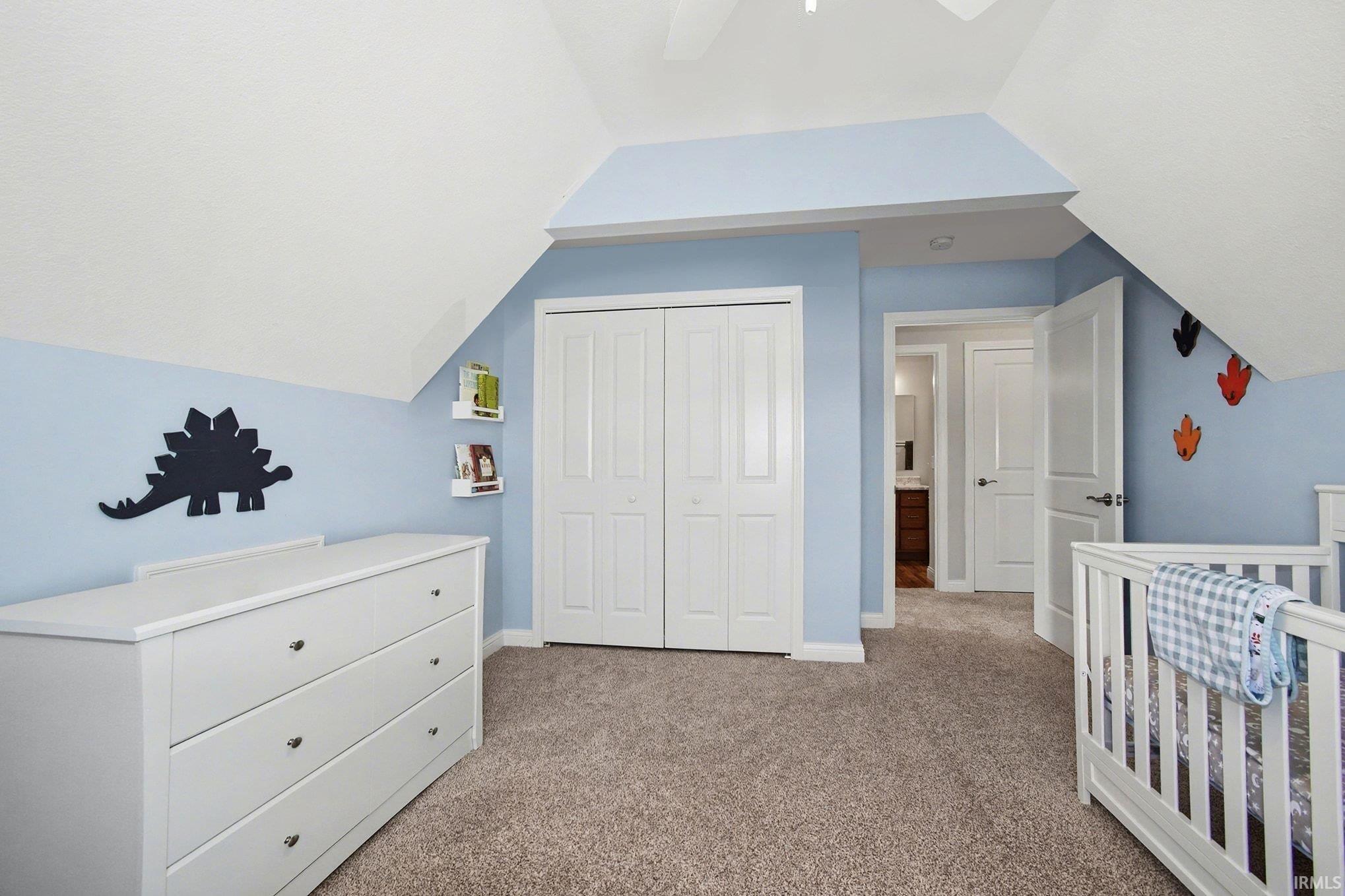 Bedroom with a nursery area, a closet, vaulted ceiling, light carpet, and a ceiling fan