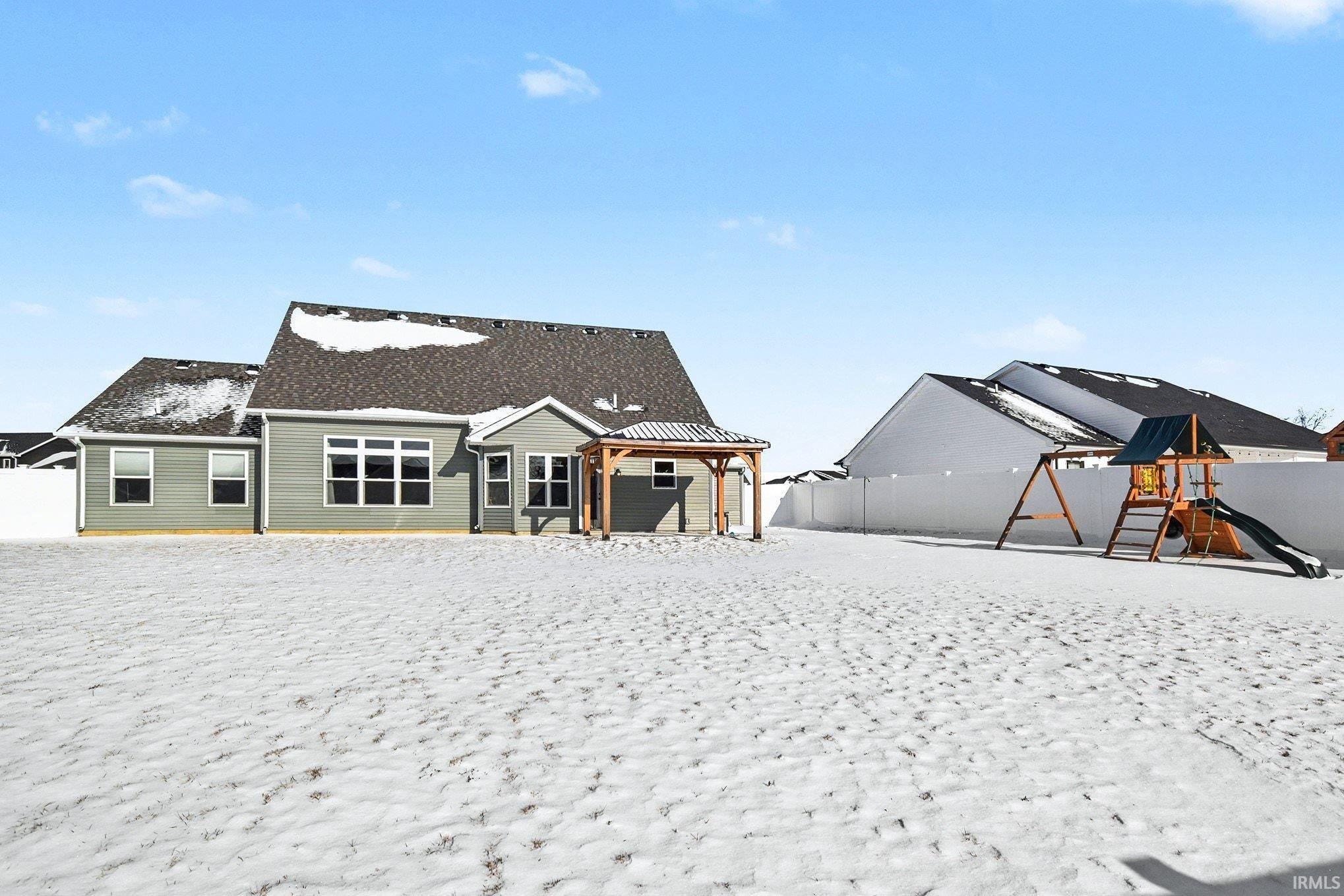 Snow covered back of property featuring a playground, a gazebo, a patio area, and a fenced backyard