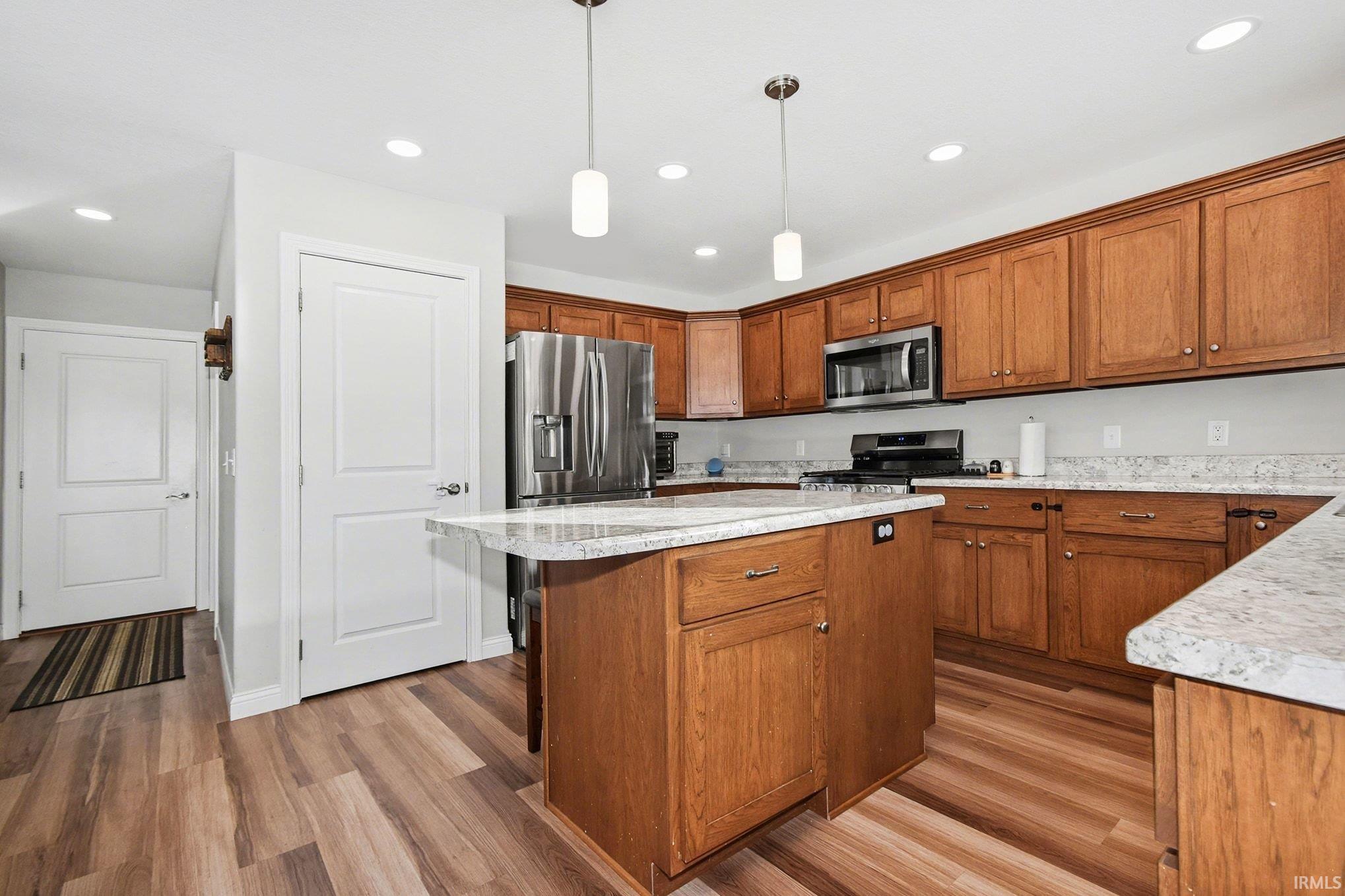 Kitchen featuring brown cabinets, a kitchen island, decorative light fixtures, light wood-style flooring, and appliances with stainless steel finishes