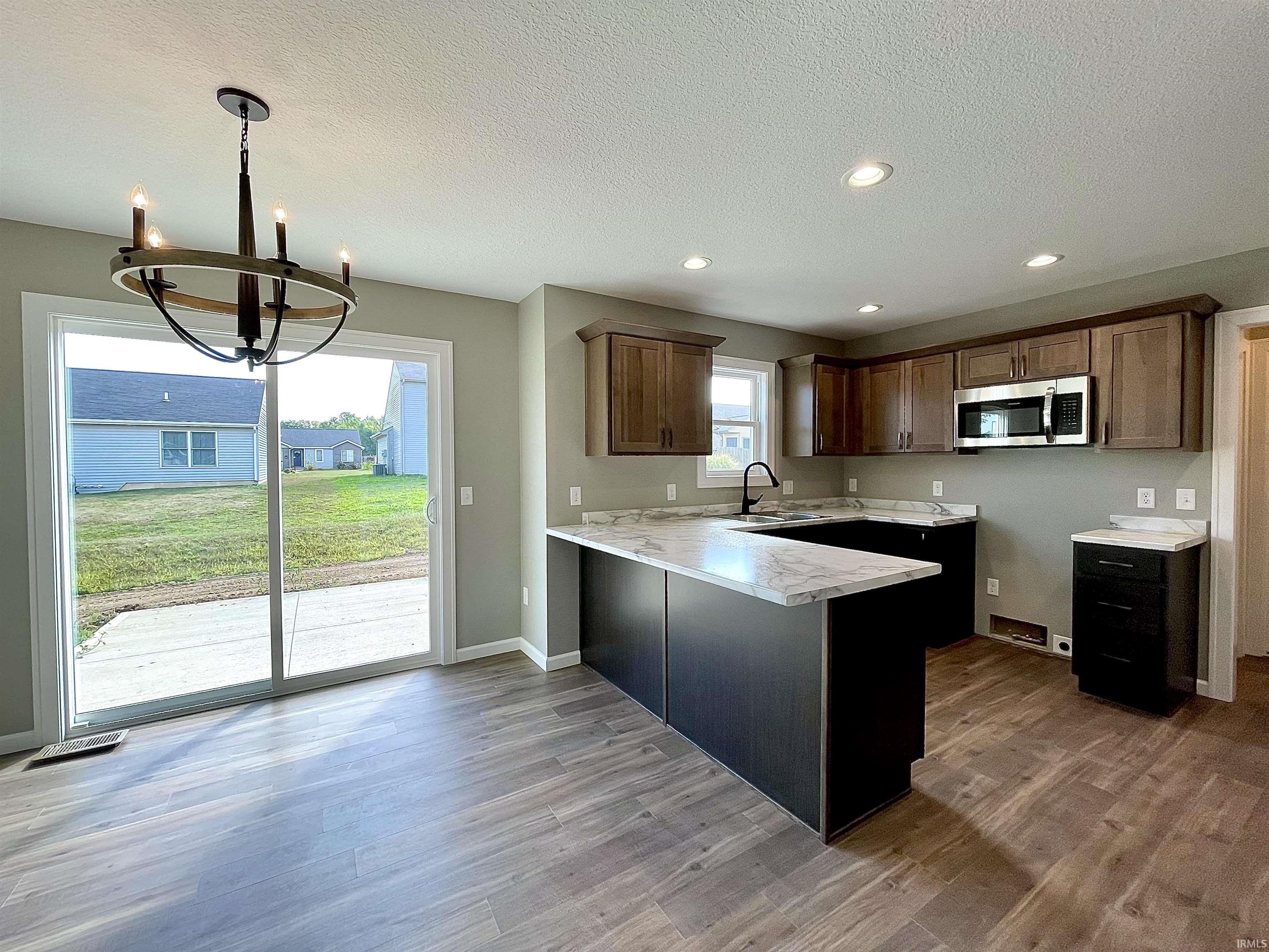 Kitchen with light countertops, a peninsula, stainless steel microwave, a chandelier, and recessed lighting