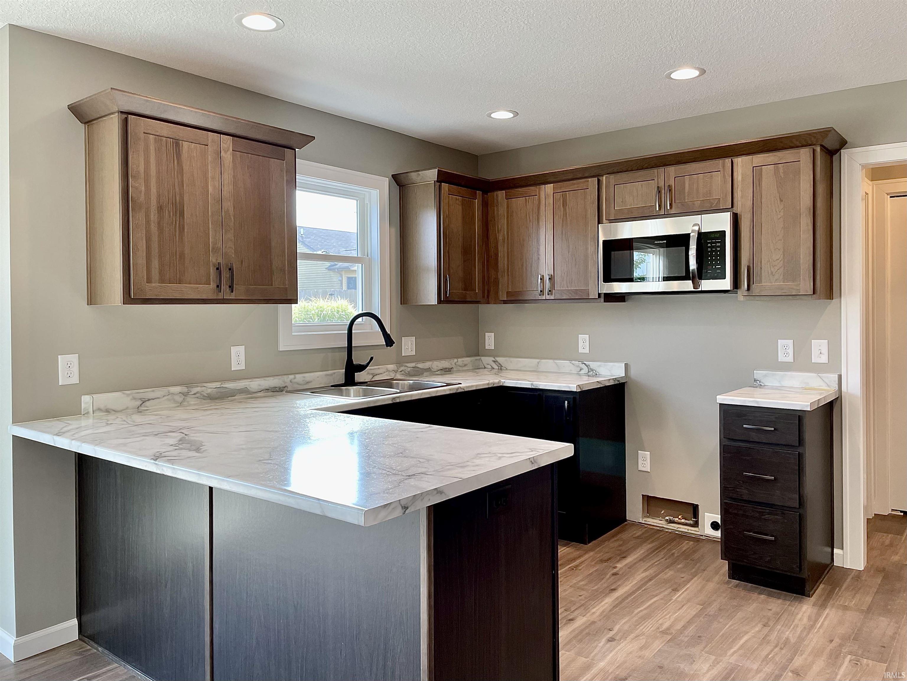Kitchen with a peninsula, light countertops, stainless steel microwave, light wood-style flooring, and recessed lighting
