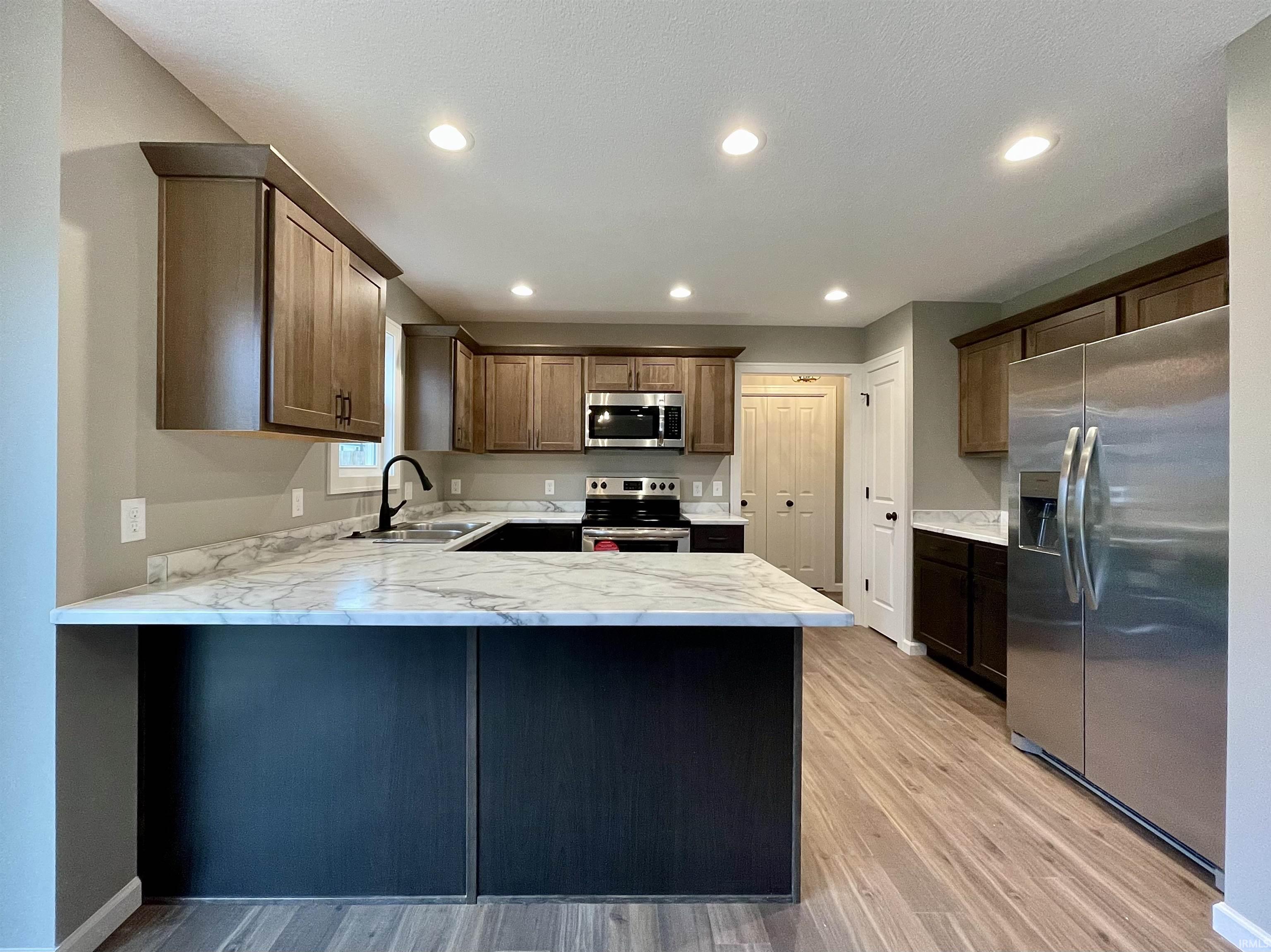 Kitchen with stainless steel appliances, a peninsula, light stone countertops, light wood finished floors, and recessed lighting