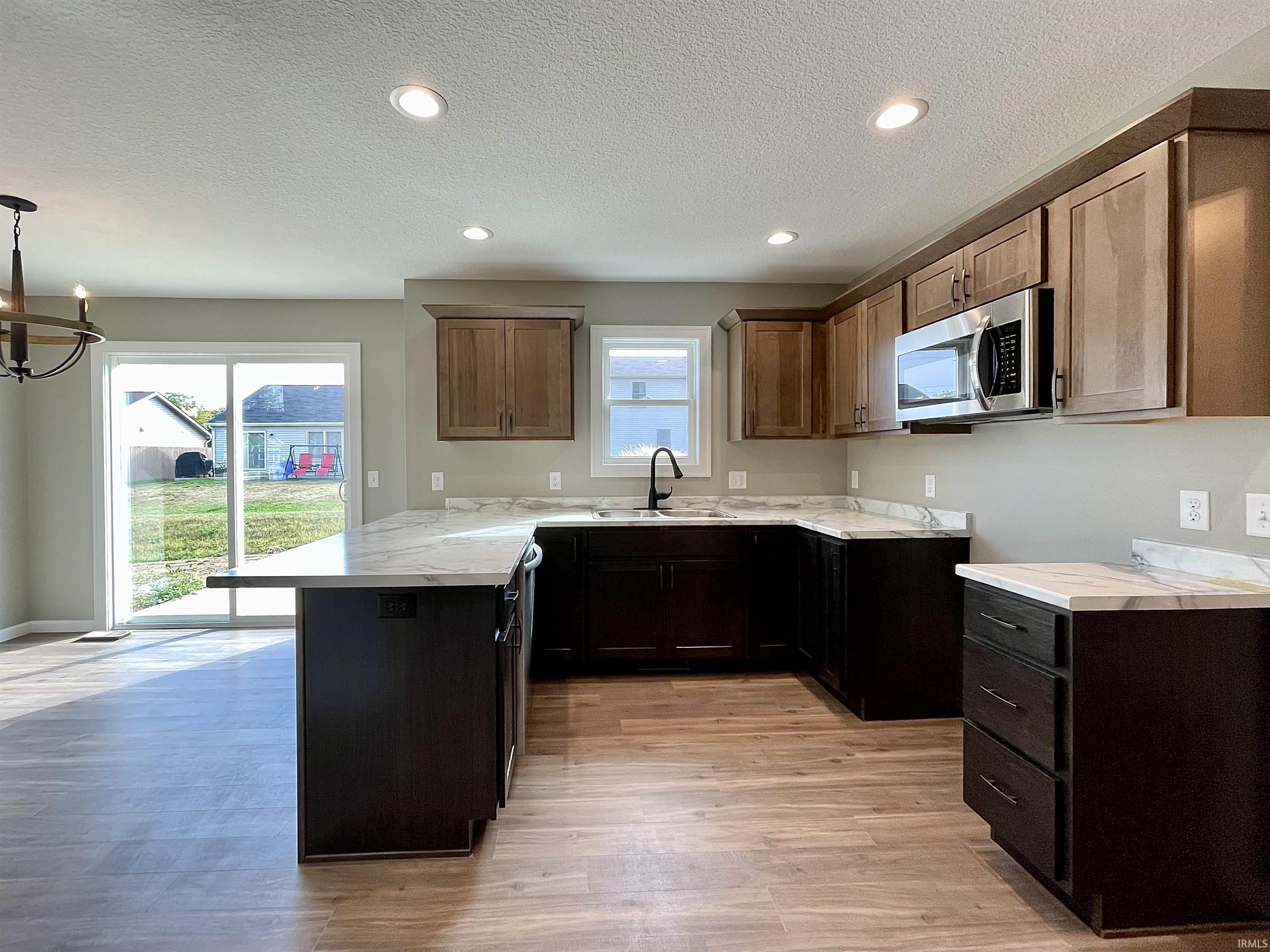 Kitchen with a peninsula, stainless steel microwave, light wood-style flooring, recessed lighting, and a textured ceiling