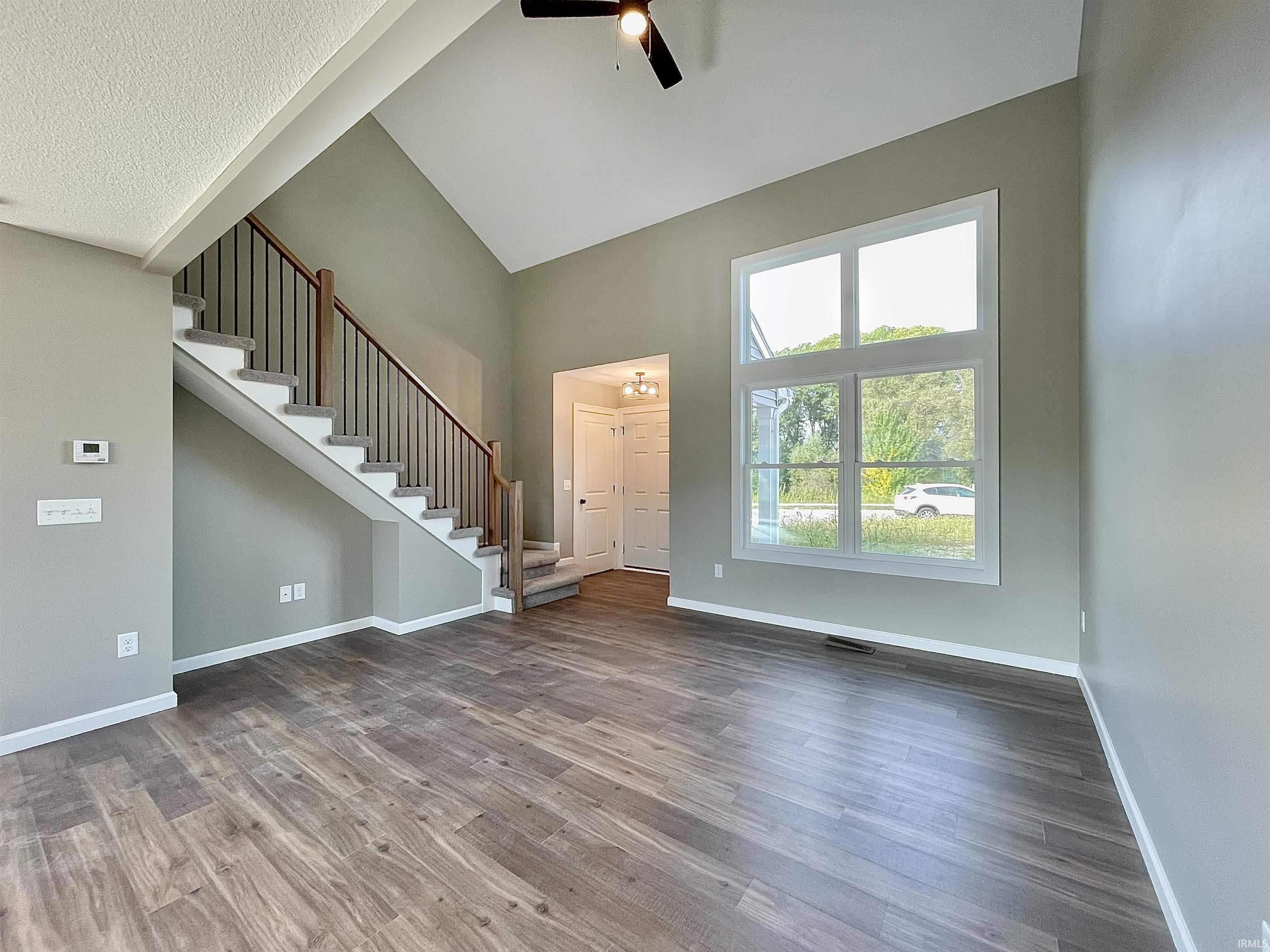 Unfurnished living room with stairs, wood finished floors, high vaulted ceiling, and a ceiling fan