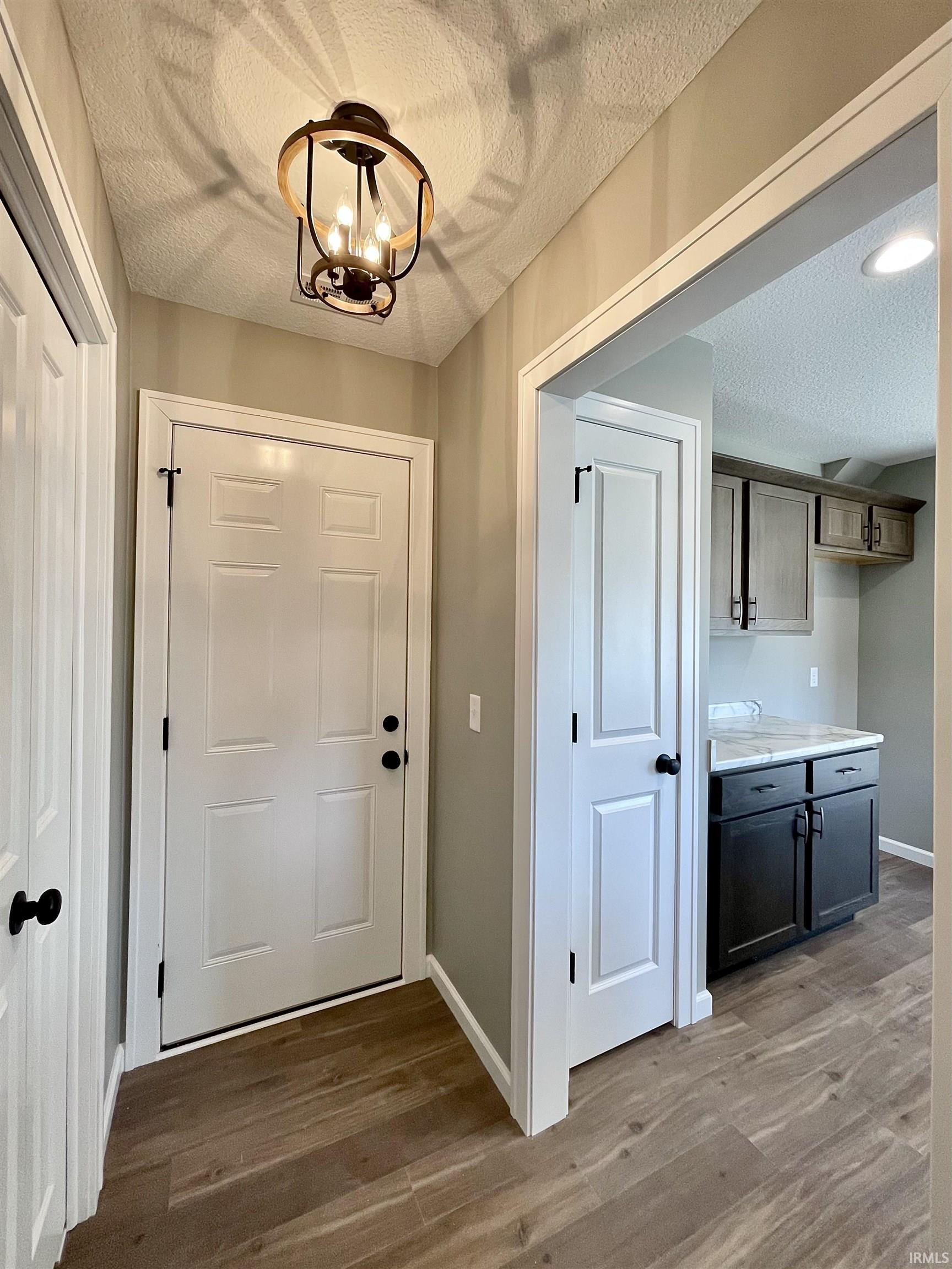 Doorway featuring a textured ceiling, wood finished floors, and a chandelier