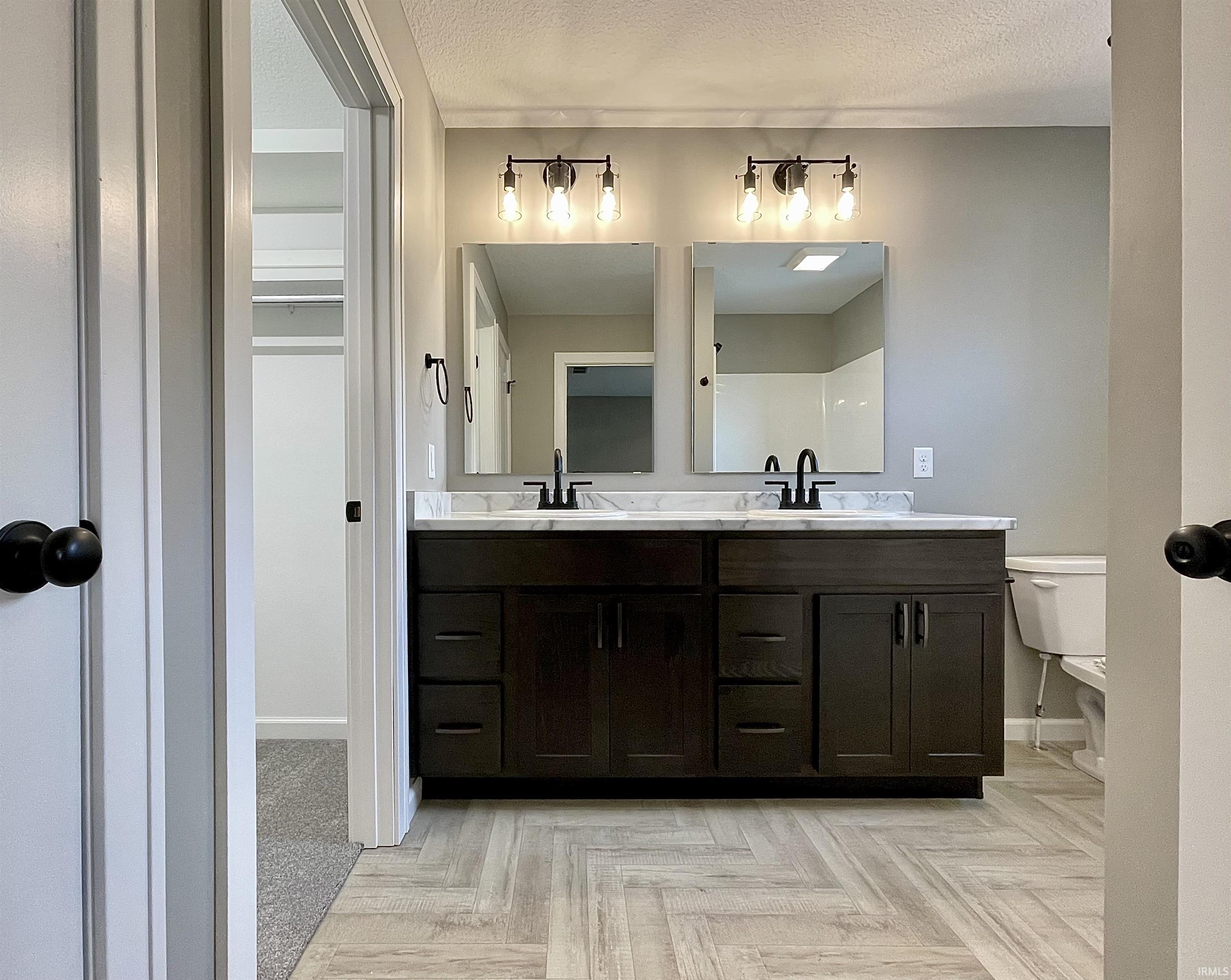 Full bath with double vanity, parquet floors, and a textured ceiling