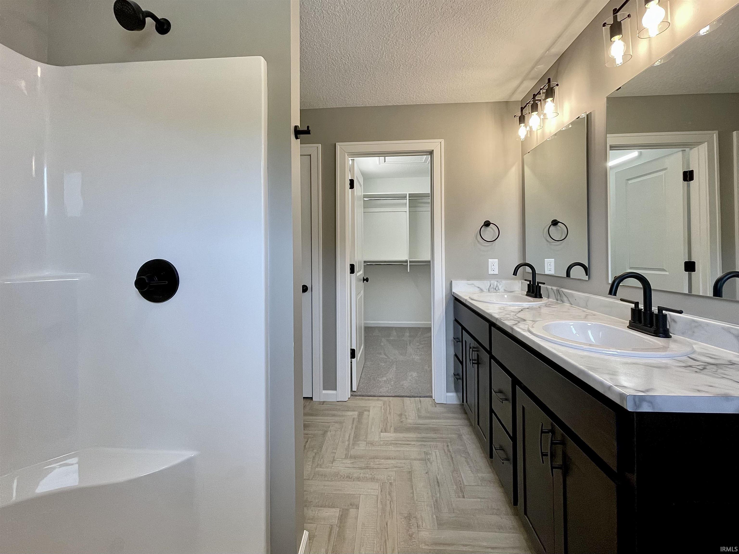 Bathroom with a walk in closet, double vanity, a textured ceiling, parquet floors, and a shower