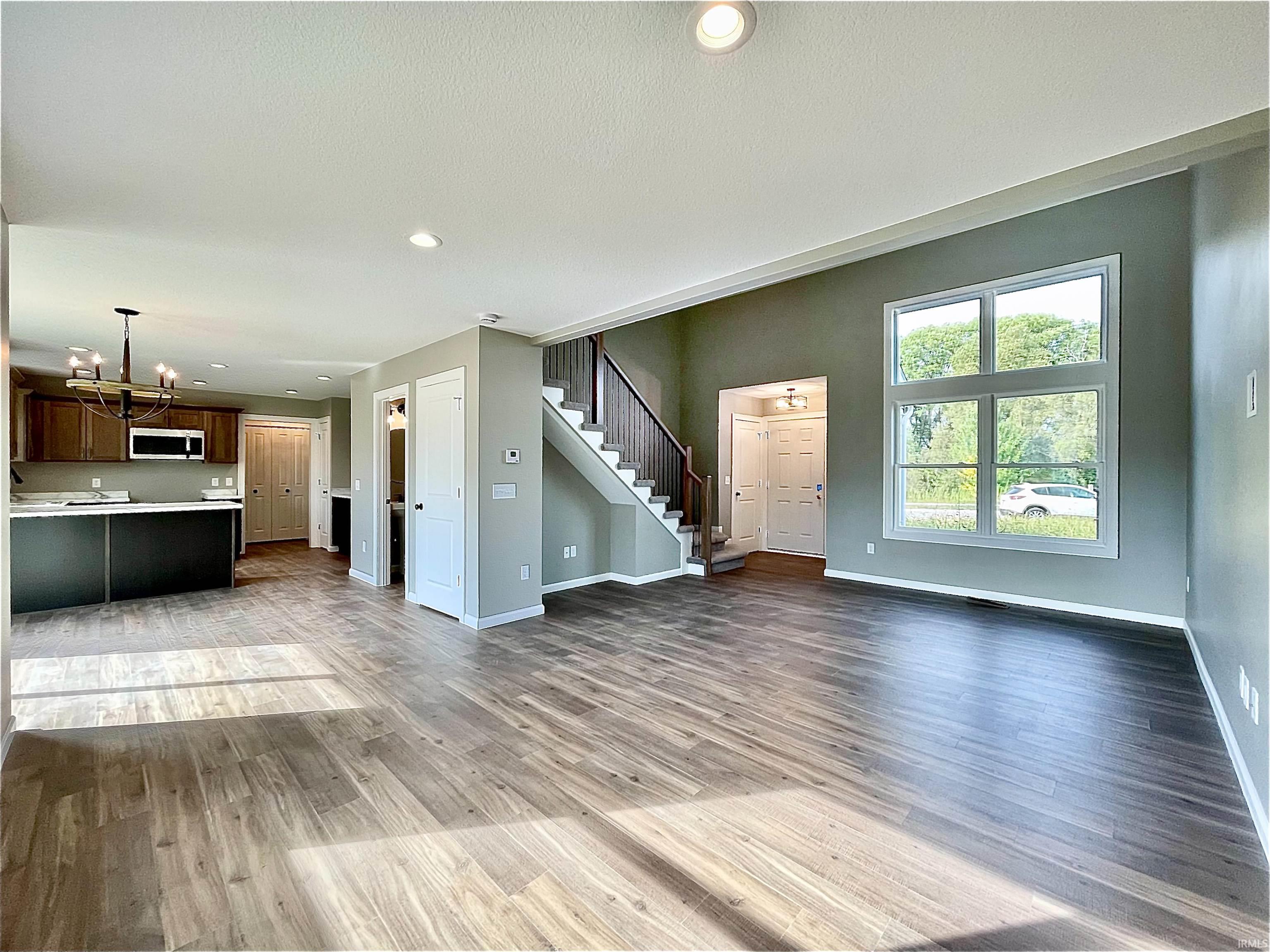 Unfurnished living room featuring light wood-type flooring, stairs, recessed lighting, and a chandelier