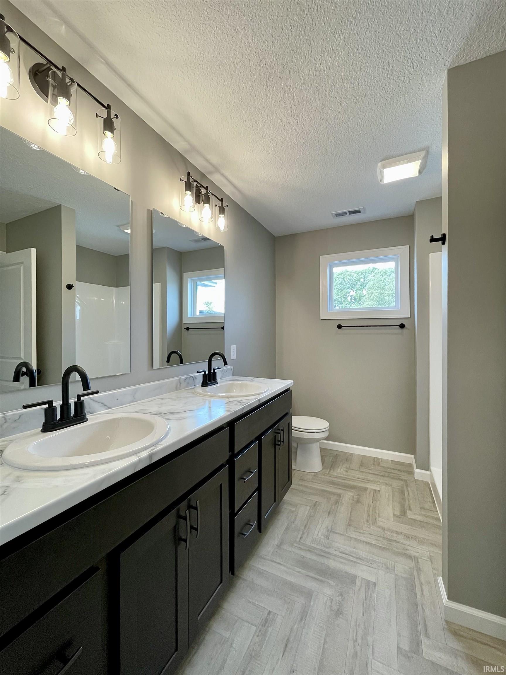 Bathroom with double vanity, parquet flooring, plenty of natural light, a textured ceiling, and a shower
