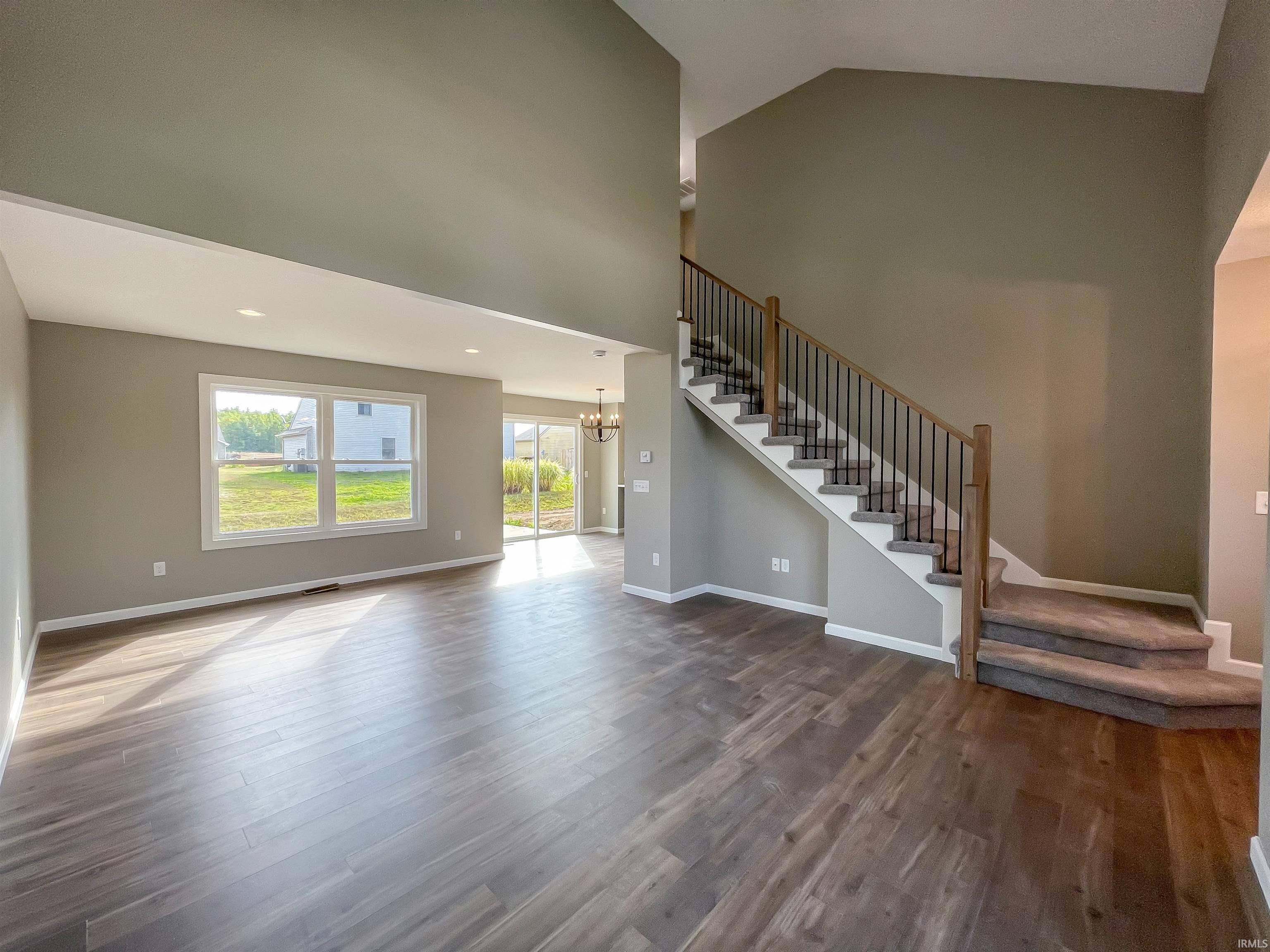 Unfurnished living room with a chandelier, dark wood-style floors, stairway, and a towering ceiling
