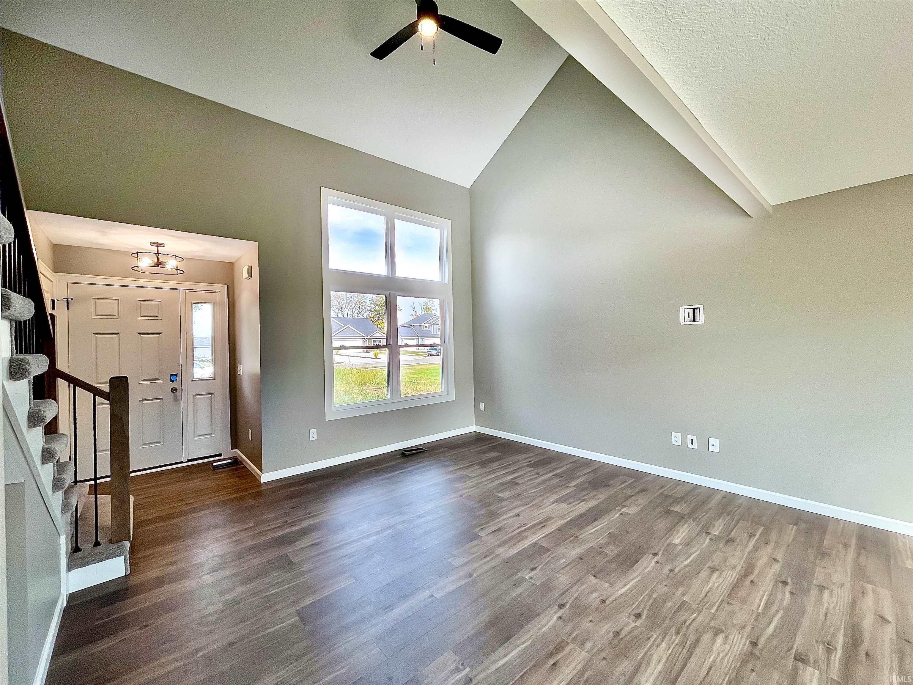 Foyer entrance with stairway, high vaulted ceiling, dark wood finished floors, and a ceiling fan