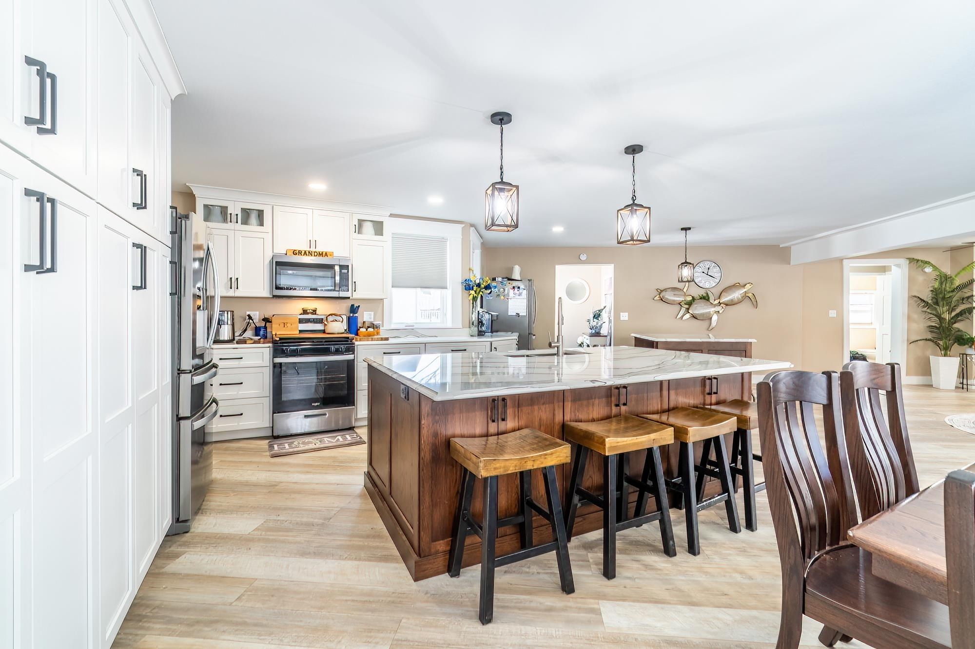 Kitchen featuring appliances with stainless steel finishes, glass insert cabinets, hanging light fixtures, an island with sink, and white cabinets