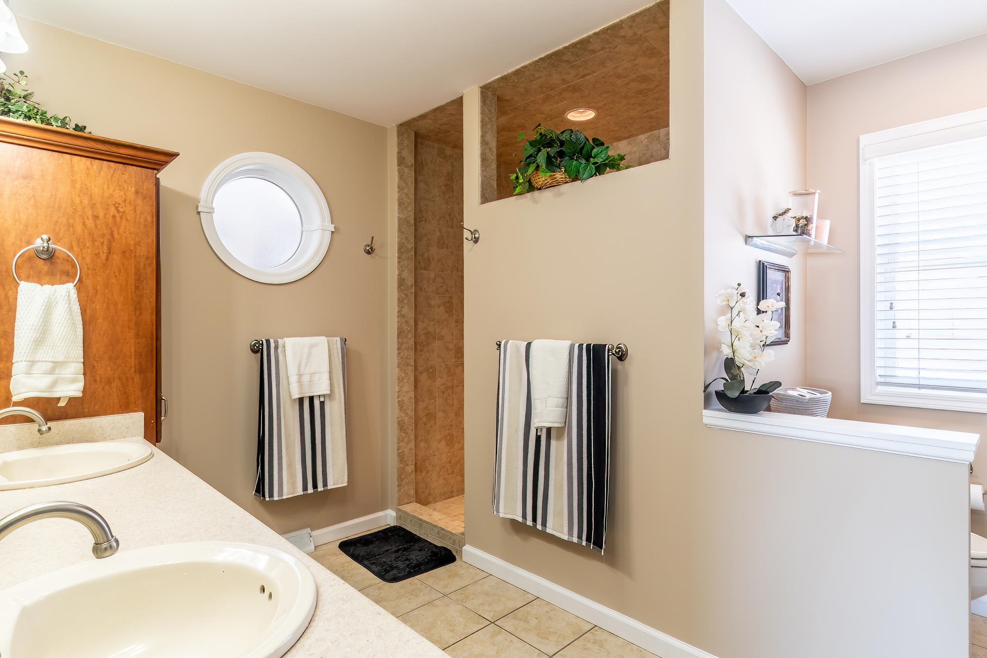 Bathroom with double vanity, light tile patterned flooring, and a walk in shower