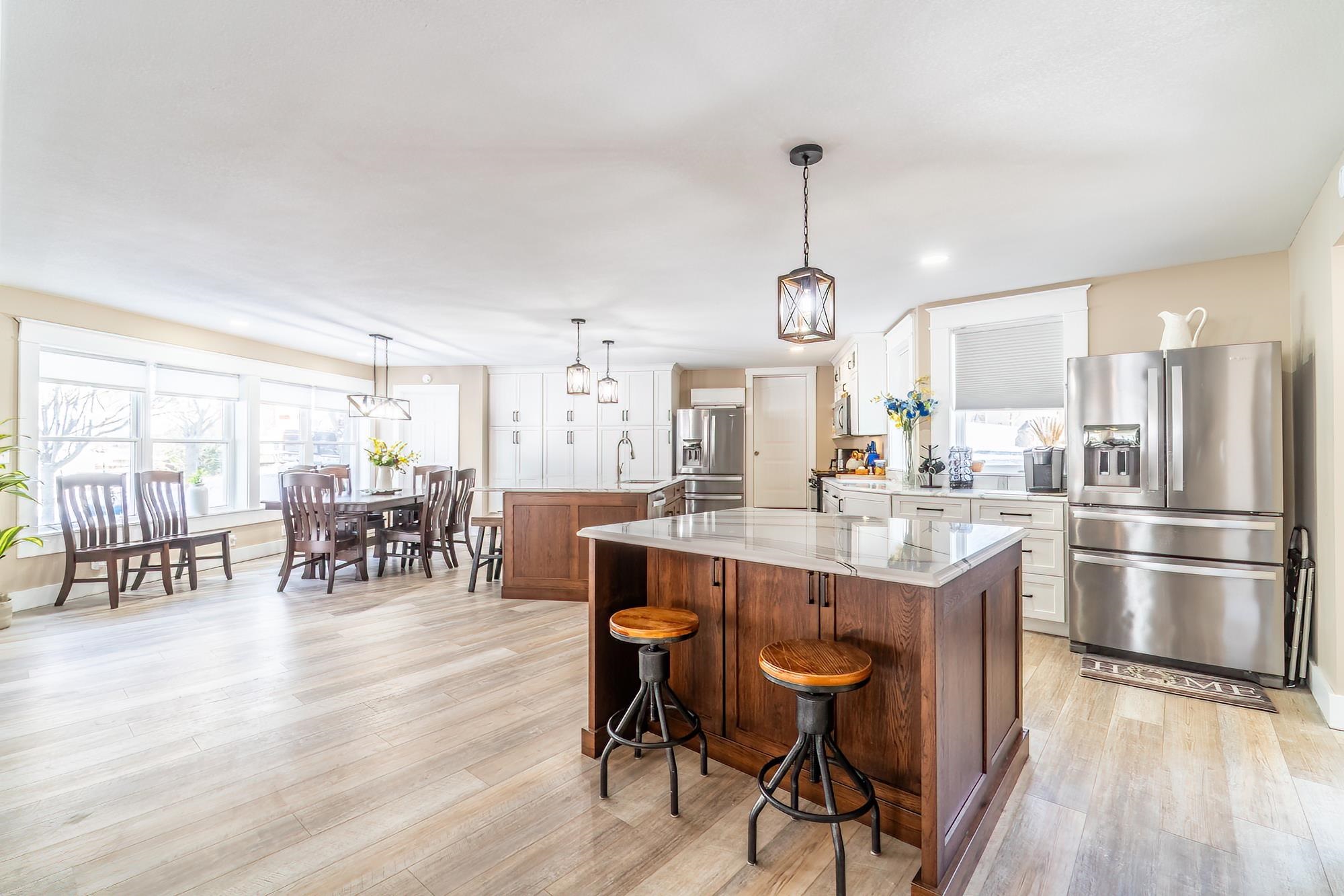 Kitchen featuring stainless steel fridge with ice dispenser, white cabinets, hanging light fixtures, and light stone counters