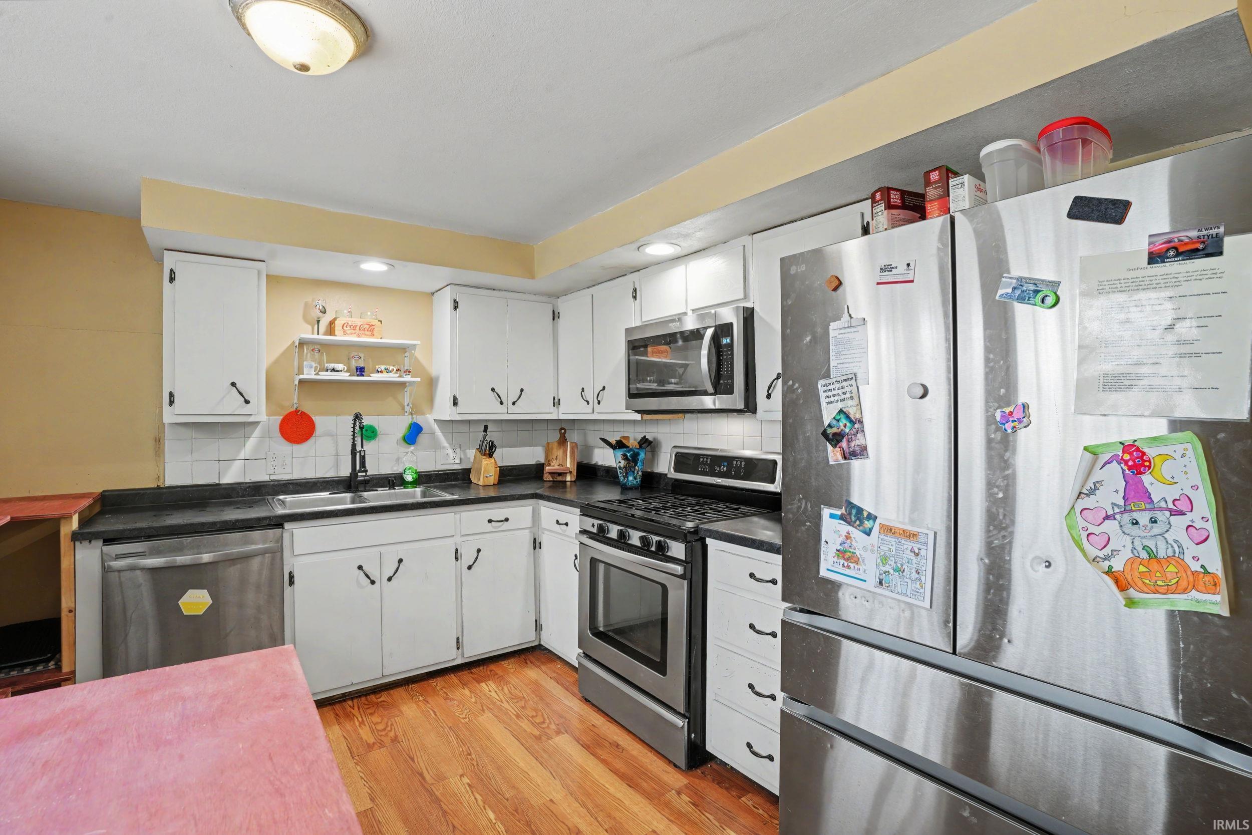 Kitchen with stainless steel appliances, dark countertops, light wood finished floors, white cabinets, and open shelves