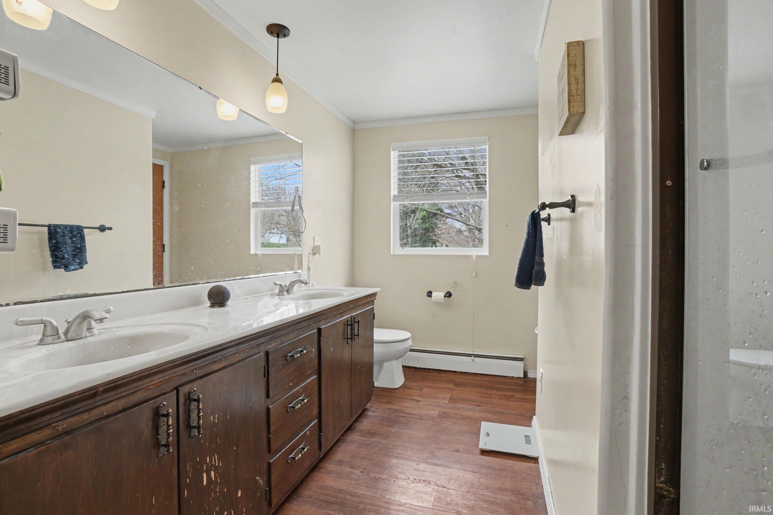Bathroom with dark wood-style flooring, double vanity, a baseboard radiator, and crown molding