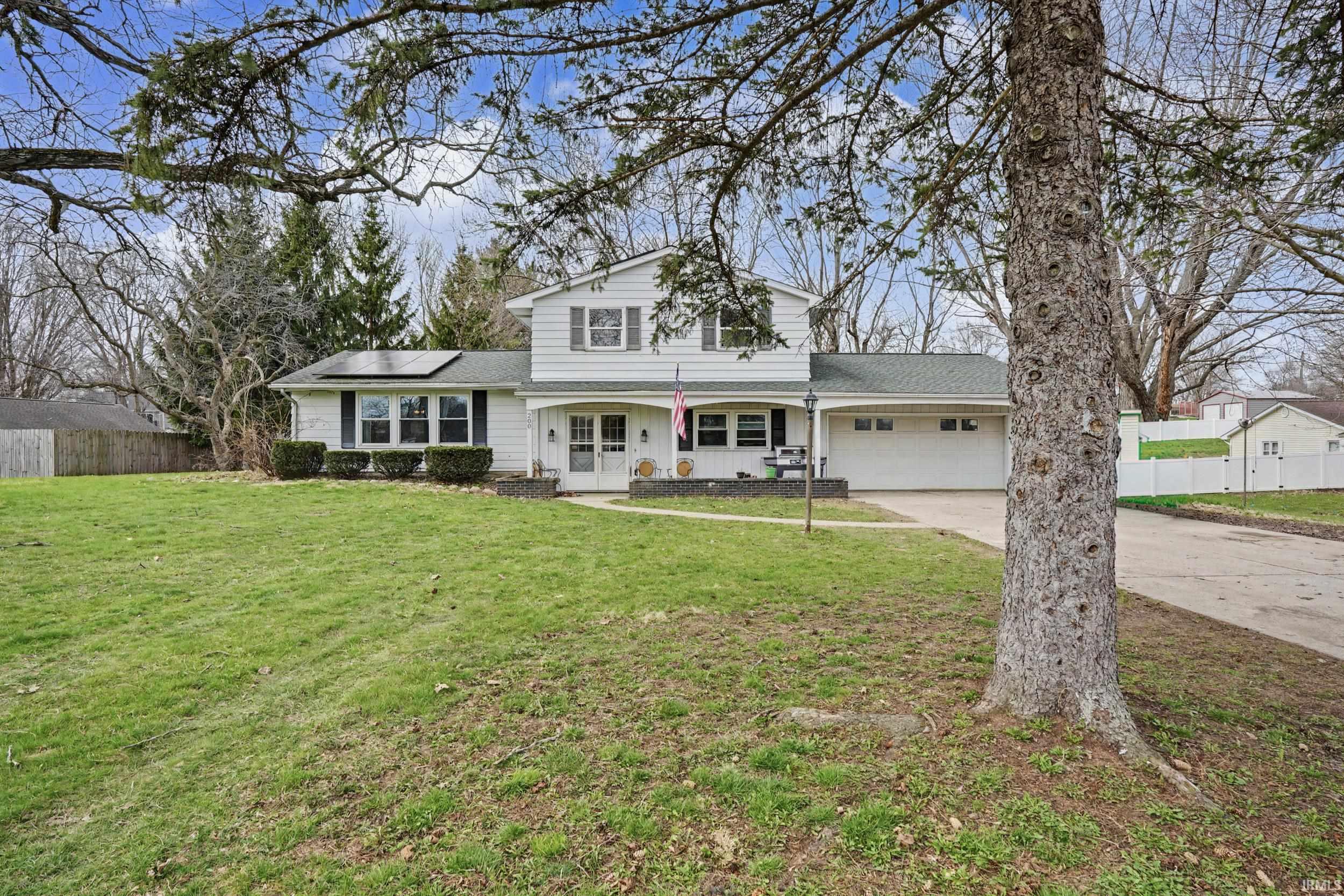 Traditional home featuring solar panels, a porch, a shingled roof, and concrete driveway
