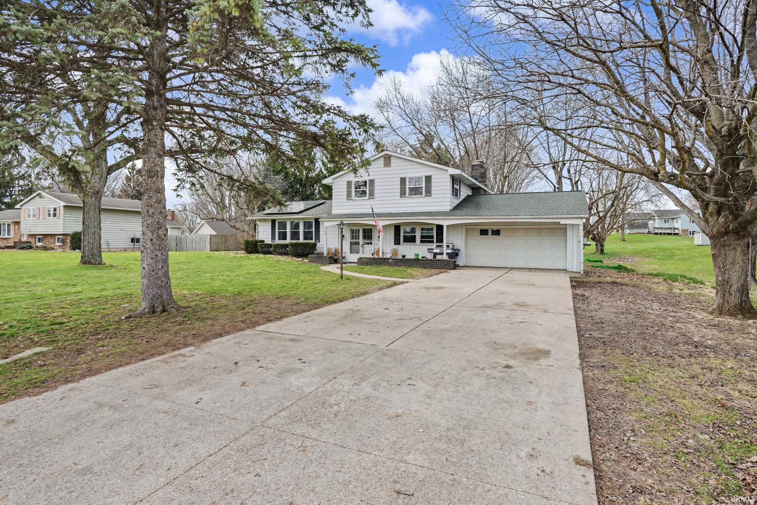 Traditional-style home featuring covered porch, a garage, driveway, a chimney, and a shingled roof