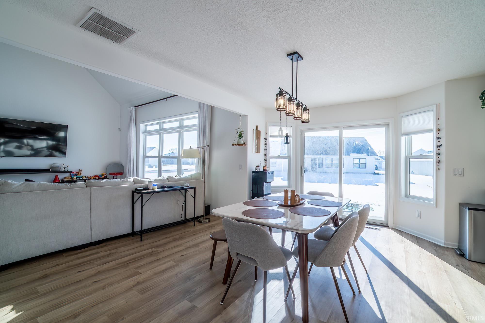 Dining room with wood finished floors, a textured ceiling, and vaulted ceiling