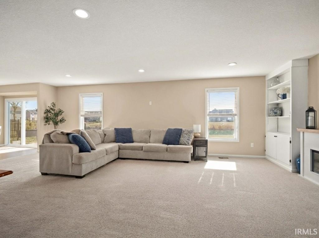 Carpeted living room with plenty of natural light, a glass covered fireplace, built in features, and recessed lighting