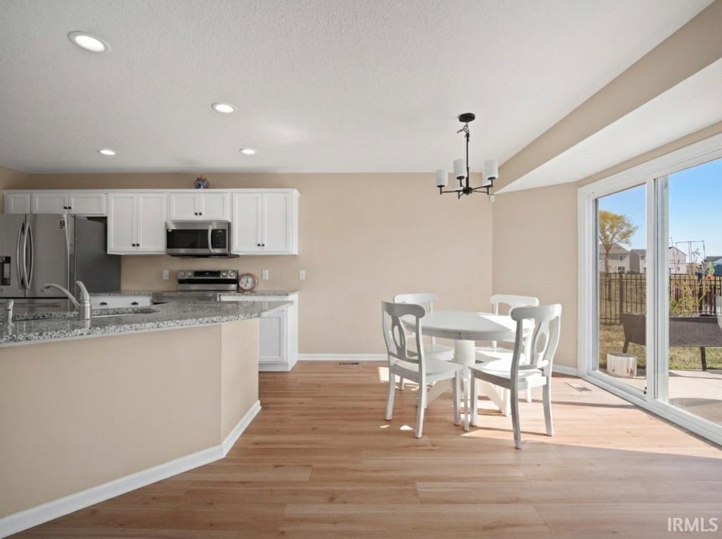 Kitchen featuring white cabinets, appliances with stainless steel finishes, light wood-style floors, decorative light fixtures, and recessed lighting