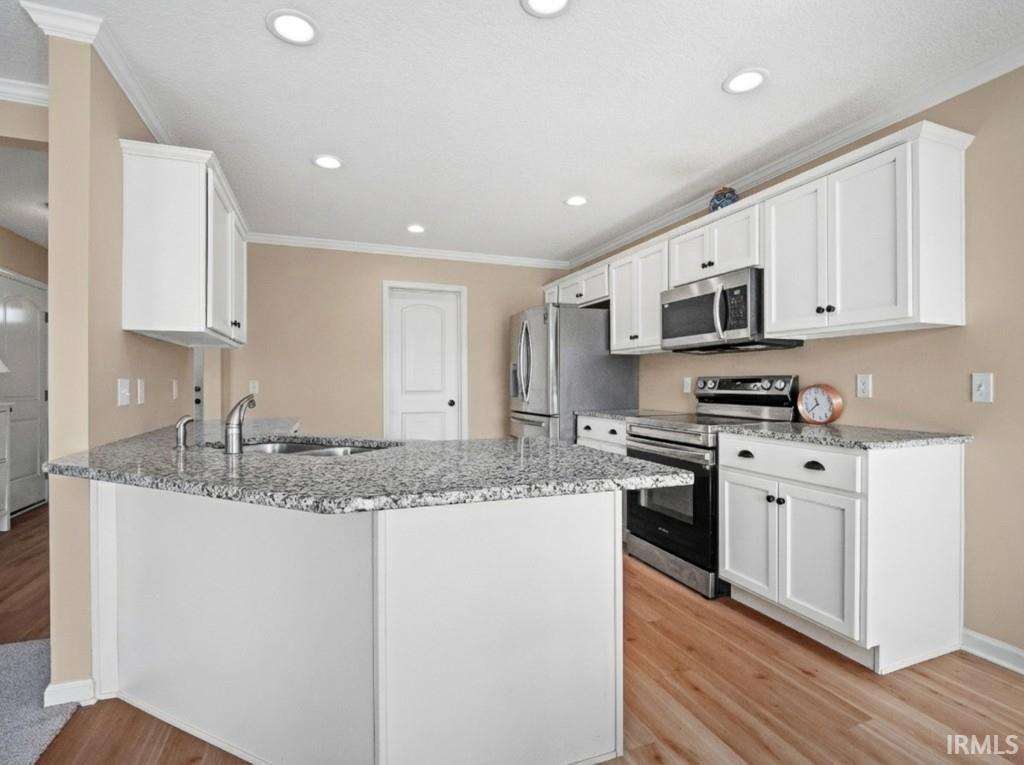 Kitchen featuring stainless steel appliances, white cabinets, a peninsula, light stone countertops, and crown molding