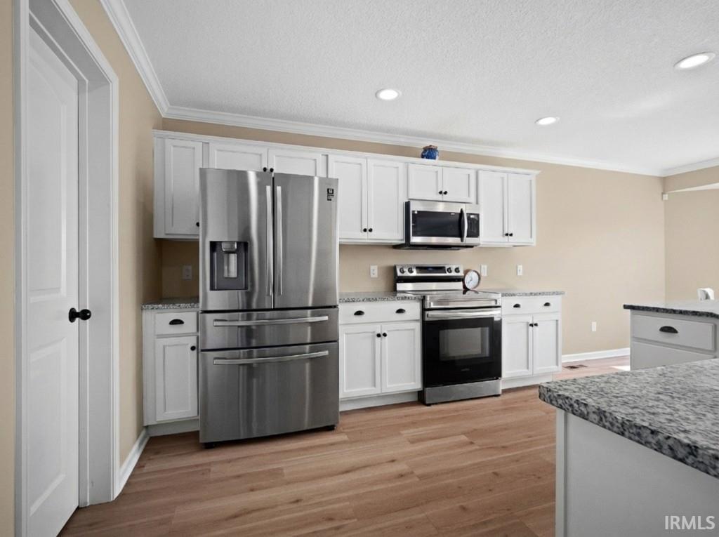 Kitchen with stainless steel appliances, ornamental molding, white cabinets, light wood-style floors, and recessed lighting