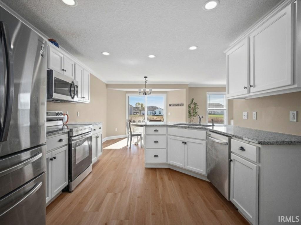 Kitchen with appliances with stainless steel finishes, a peninsula, white cabinets, light wood-style flooring, and recessed lighting