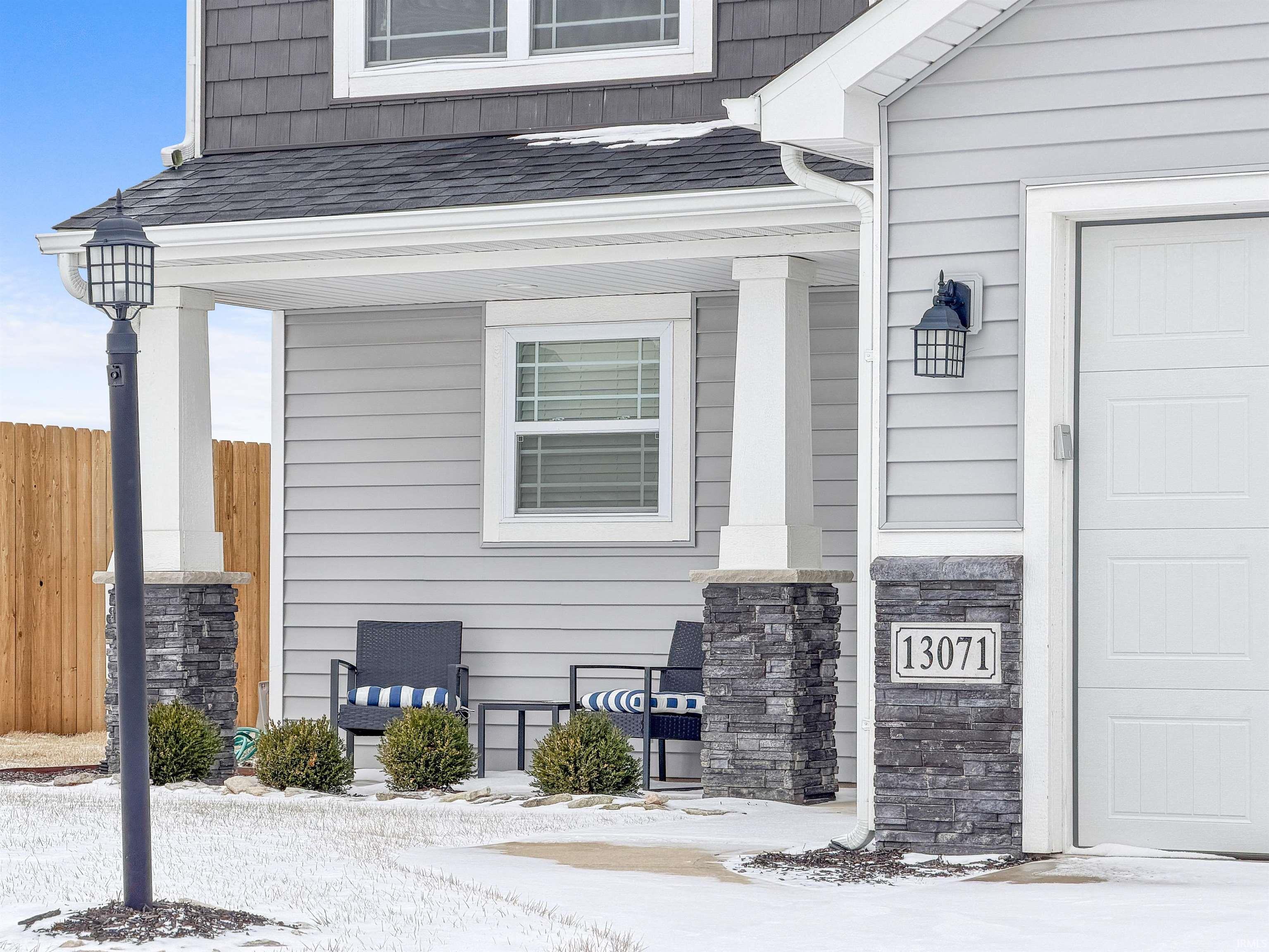 View of snowy exterior featuring roof with shingles, a garage, and covered porch