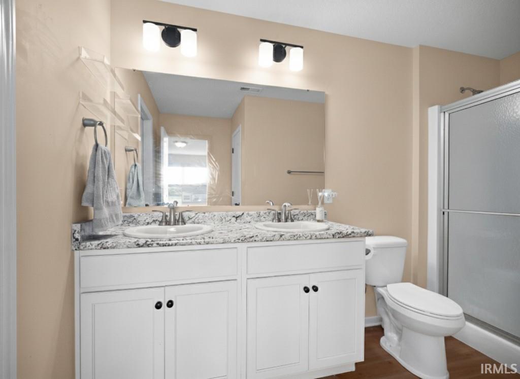 Full bath with double vanity, a stall shower, and dark wood-style flooring
